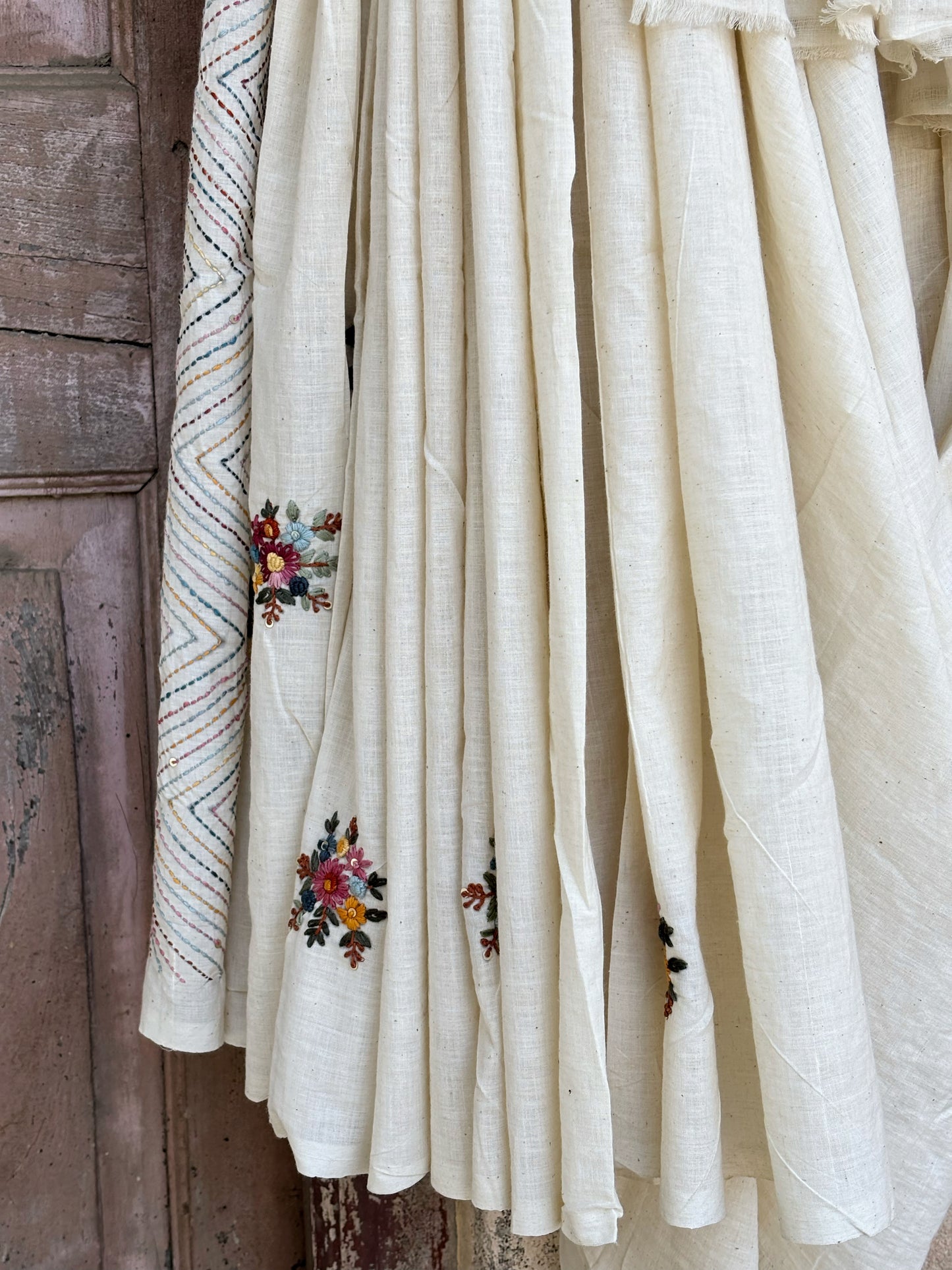 Handspun and handwoven cotton saree in natural ivory shade, featuring intricate hand embroidered floral motifs with subtle sequins. Slow made artisanal saree inspired by Basant, paired with a hand embroidered blouse piece.