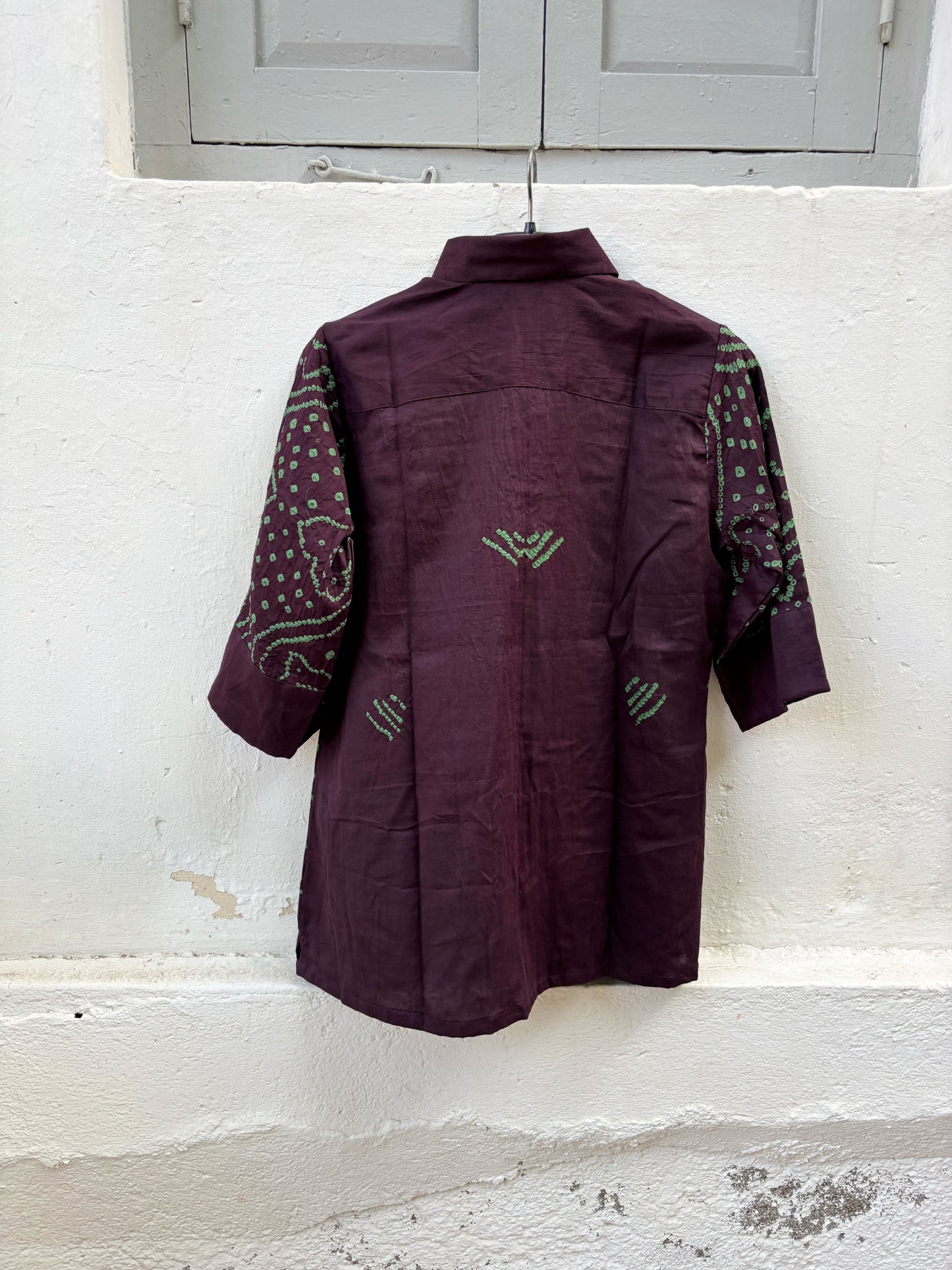 Jhankar Bandhani cotton shirt in deep jamun purple with sage green paisley motifs, classic shirt collar, folded sleeve cuffs, coconut shell buttons, and relaxed fit.