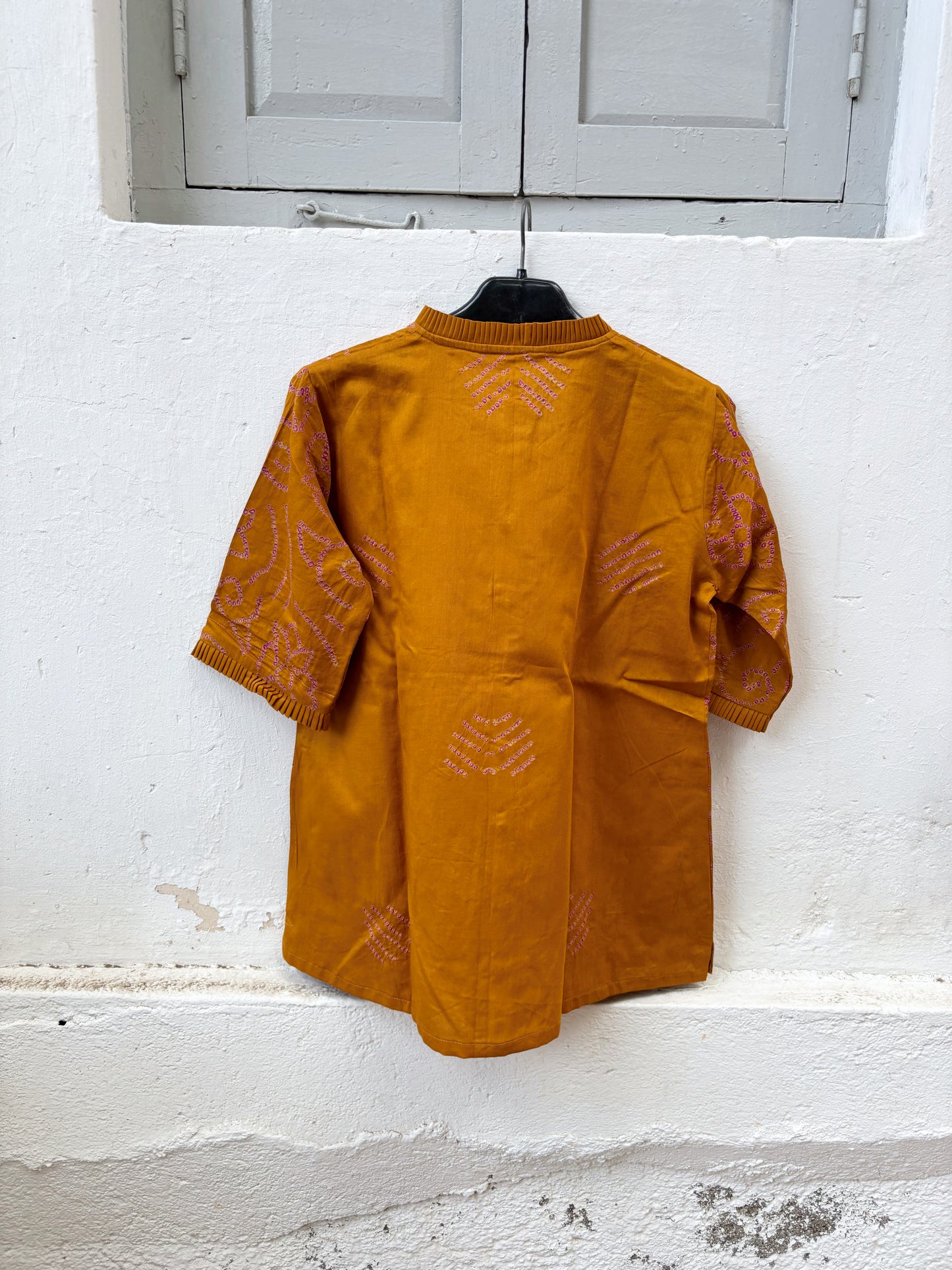 Hand tie-dyed Kesari ochre cotton Bandhani shirt with muted purple Jhankaar motifs, pleated neckline and relaxed fit.