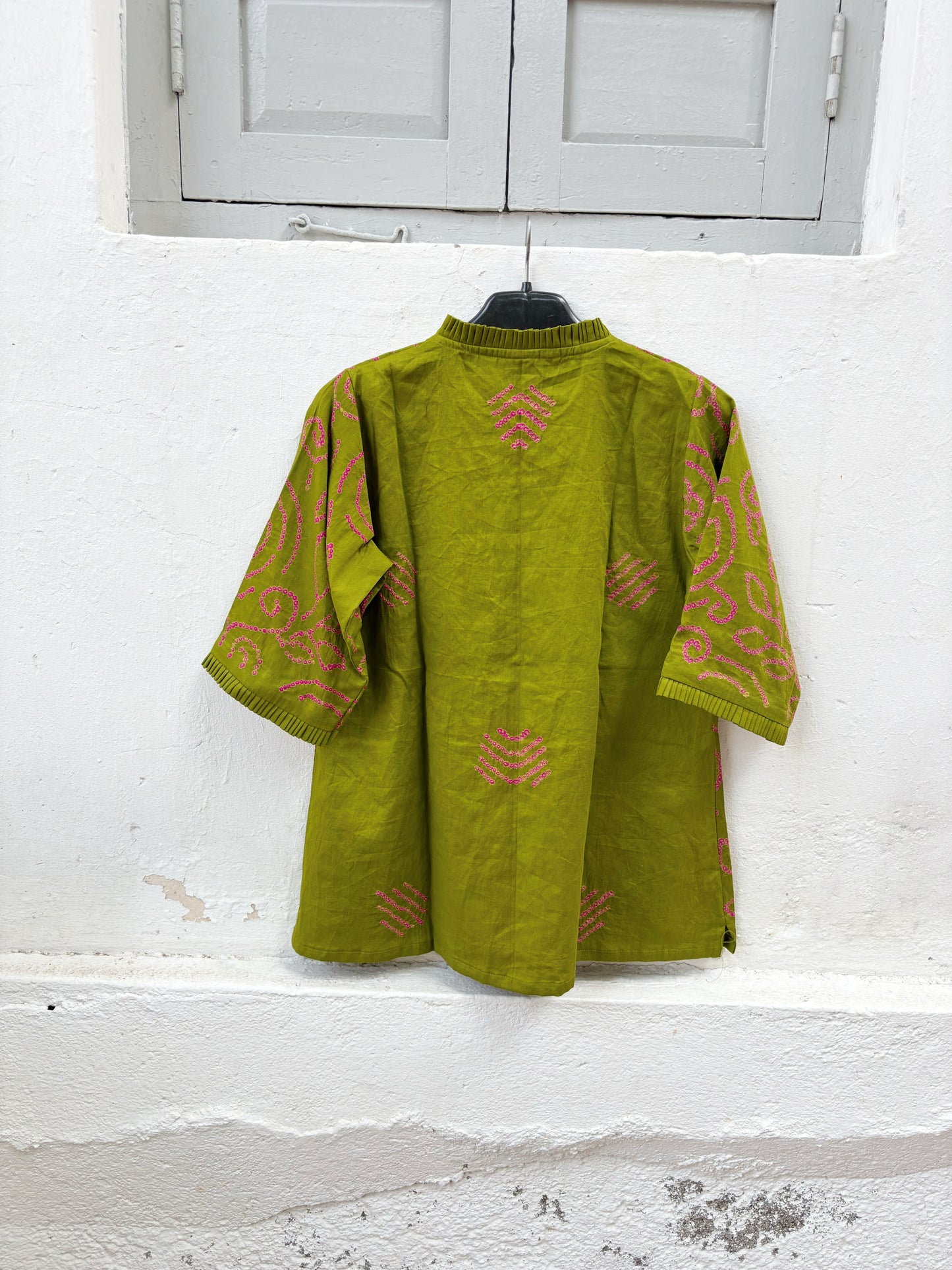 Olive green Jhankar Bandhani cotton shirt with rani pink floral and paisley motifs, pleated neckline, pleated sleeve hems, coconut shell buttons, and relaxed fit.