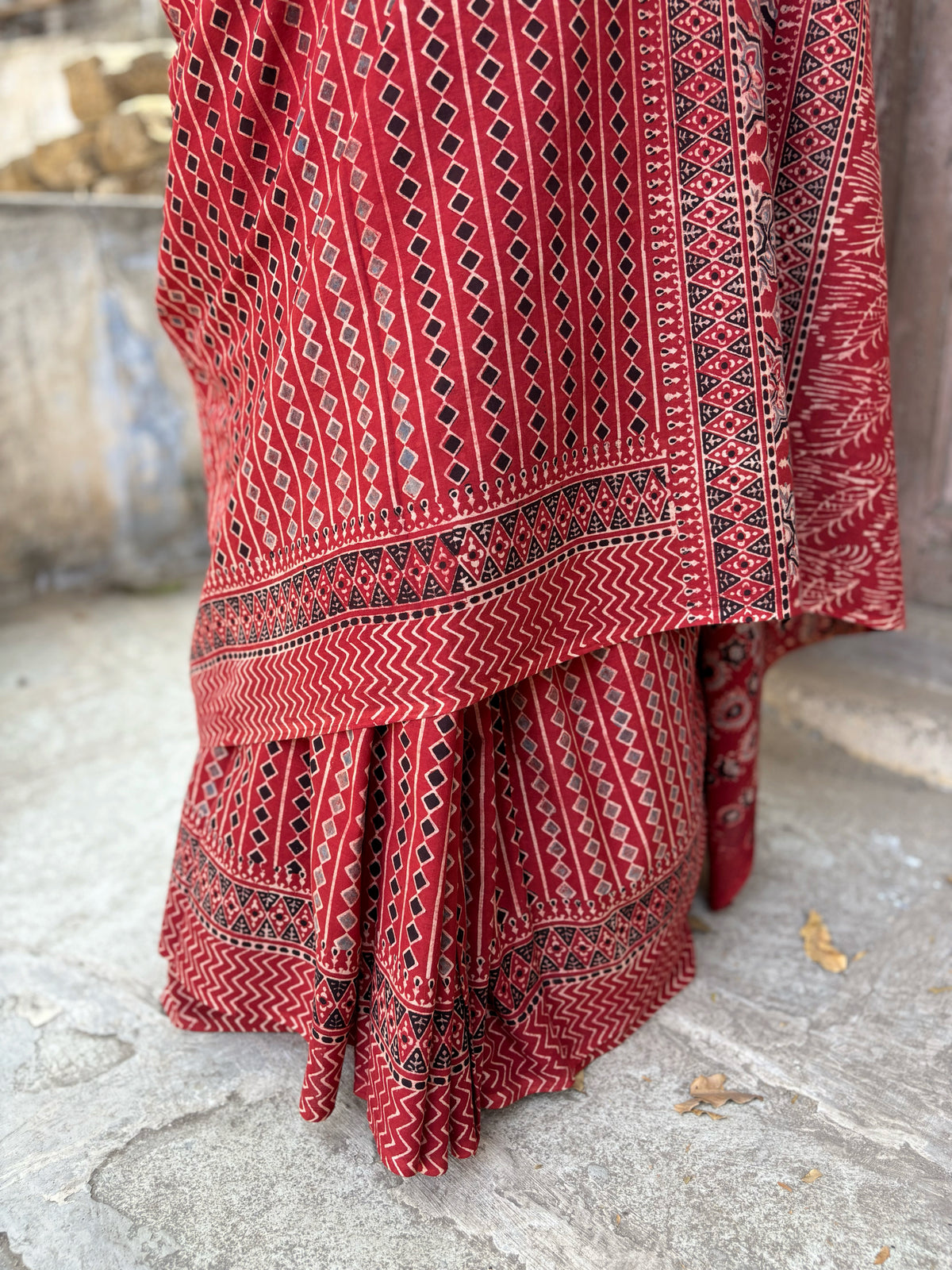 Madder dyed cotton Ajrakh hand block printed saree featuring traditional geometric motifs in red, black, and beige with detailed borders and pallu.