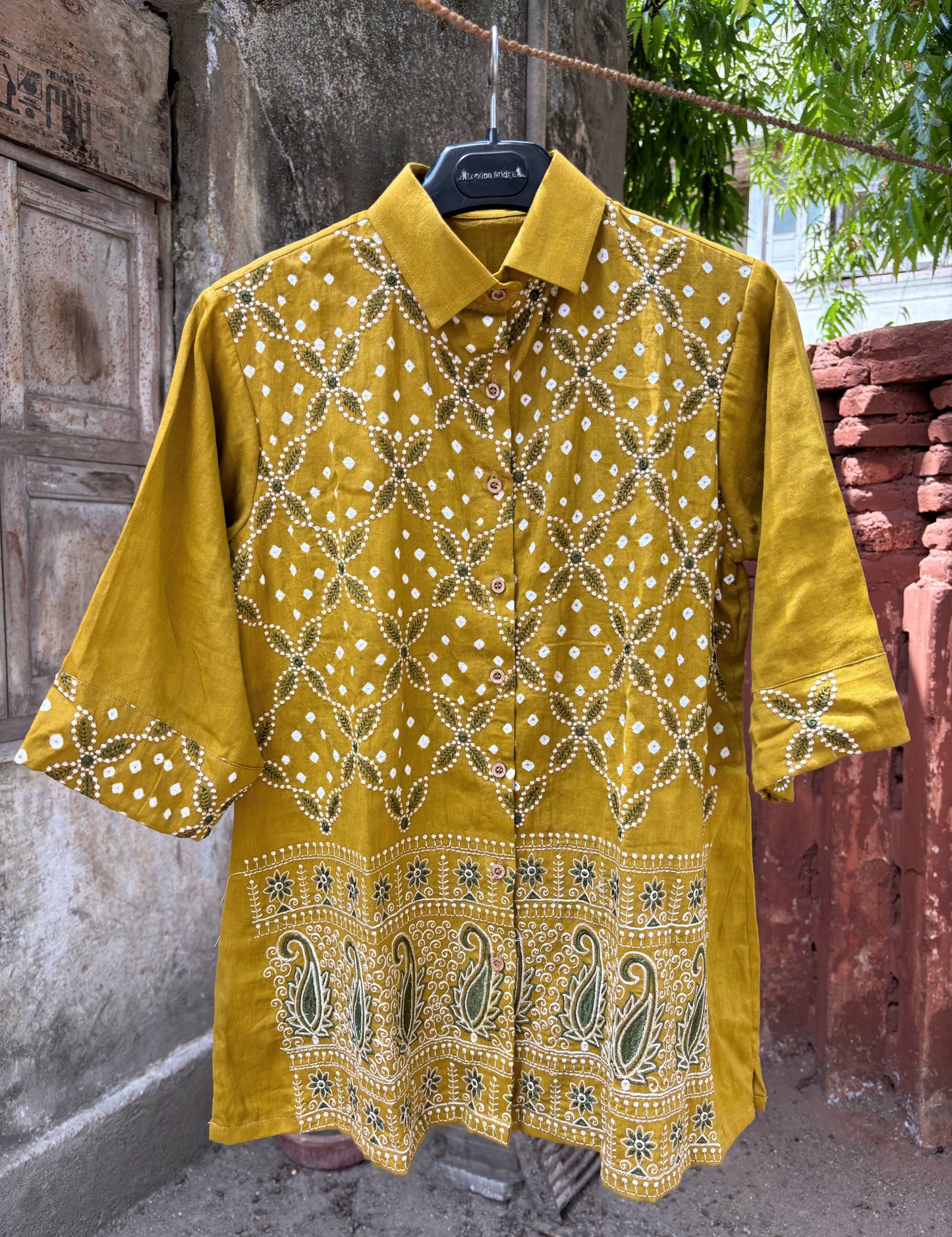 Warm mustard gold cotton satin Bandhani shirt with machine embroidered floral vine pattern, paisley border detailing, shirt collar, and relaxed fit.