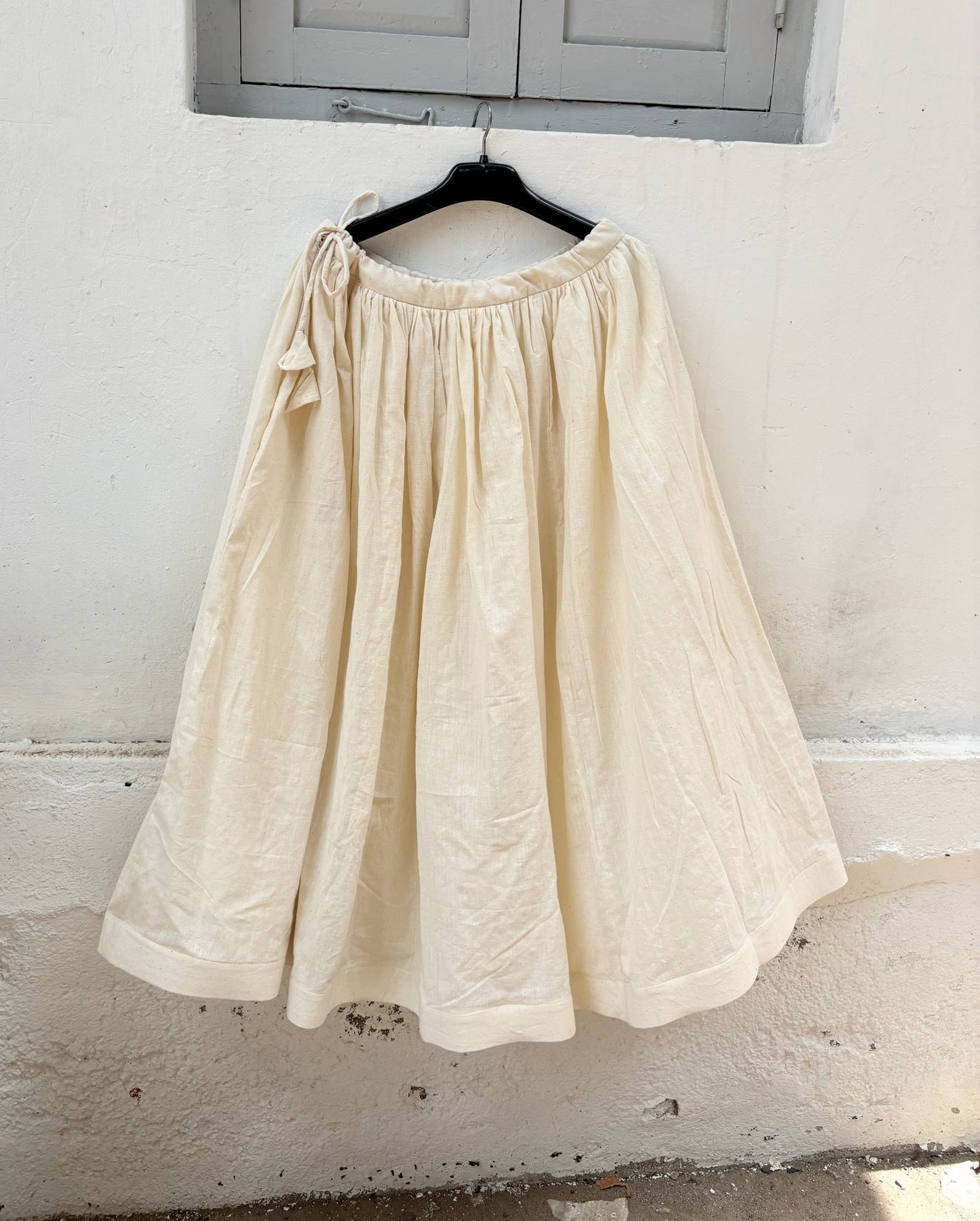 Undyed raw hand-spun and handwoven cotton gathered skirt in natural off-white with adjustable tie strings, side zipper and flowing silhouette.