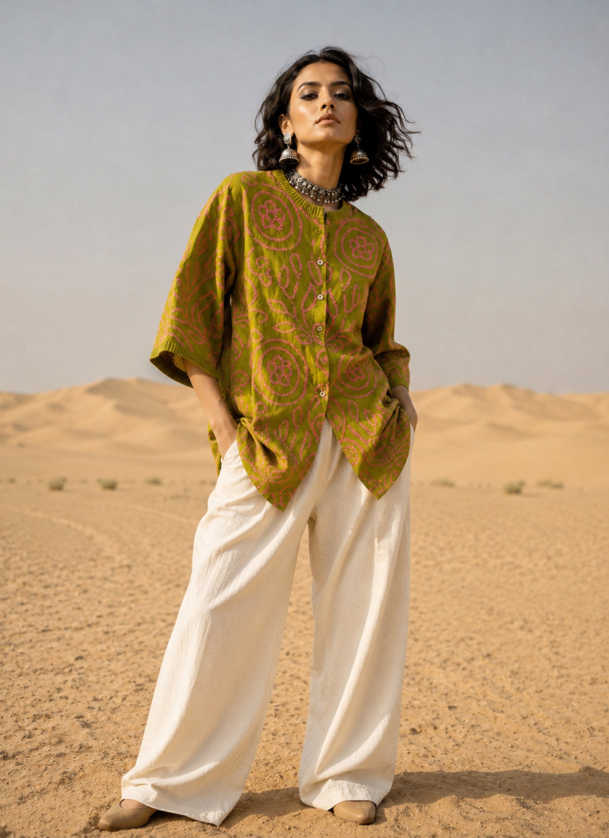 Olive green Jhankar Bandhani cotton shirt with rani pink floral and paisley motifs, pleated neckline, pleated sleeve hems, coconut shell buttons, and relaxed fit.
