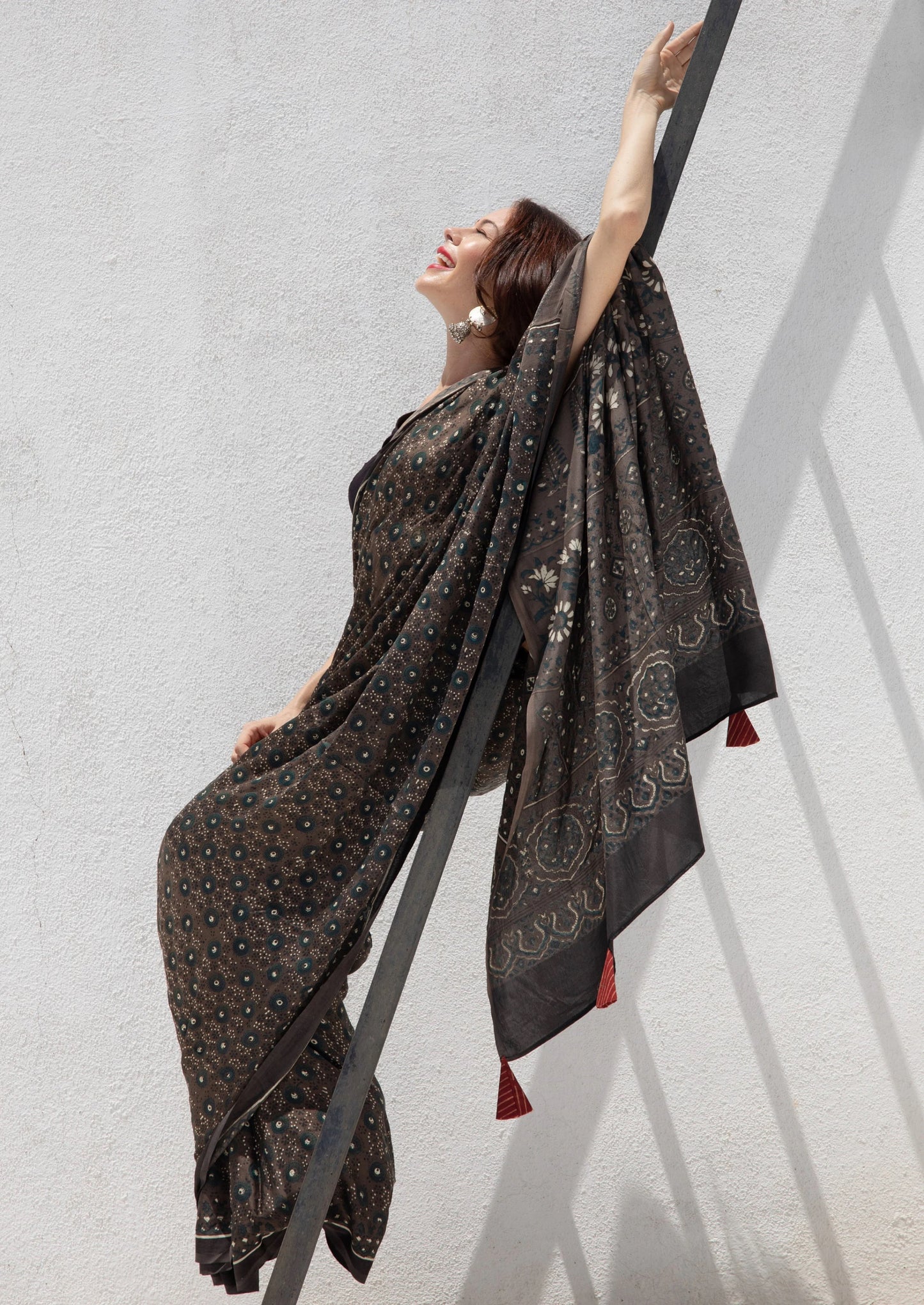 Grey Ajrakh hand block printed modal silk saree, naturally dyed and handcrafted by artisans in Gujarat, India. Features soft luxurious drape, intricate prints, tasselled pallu, and a running blouse inside.