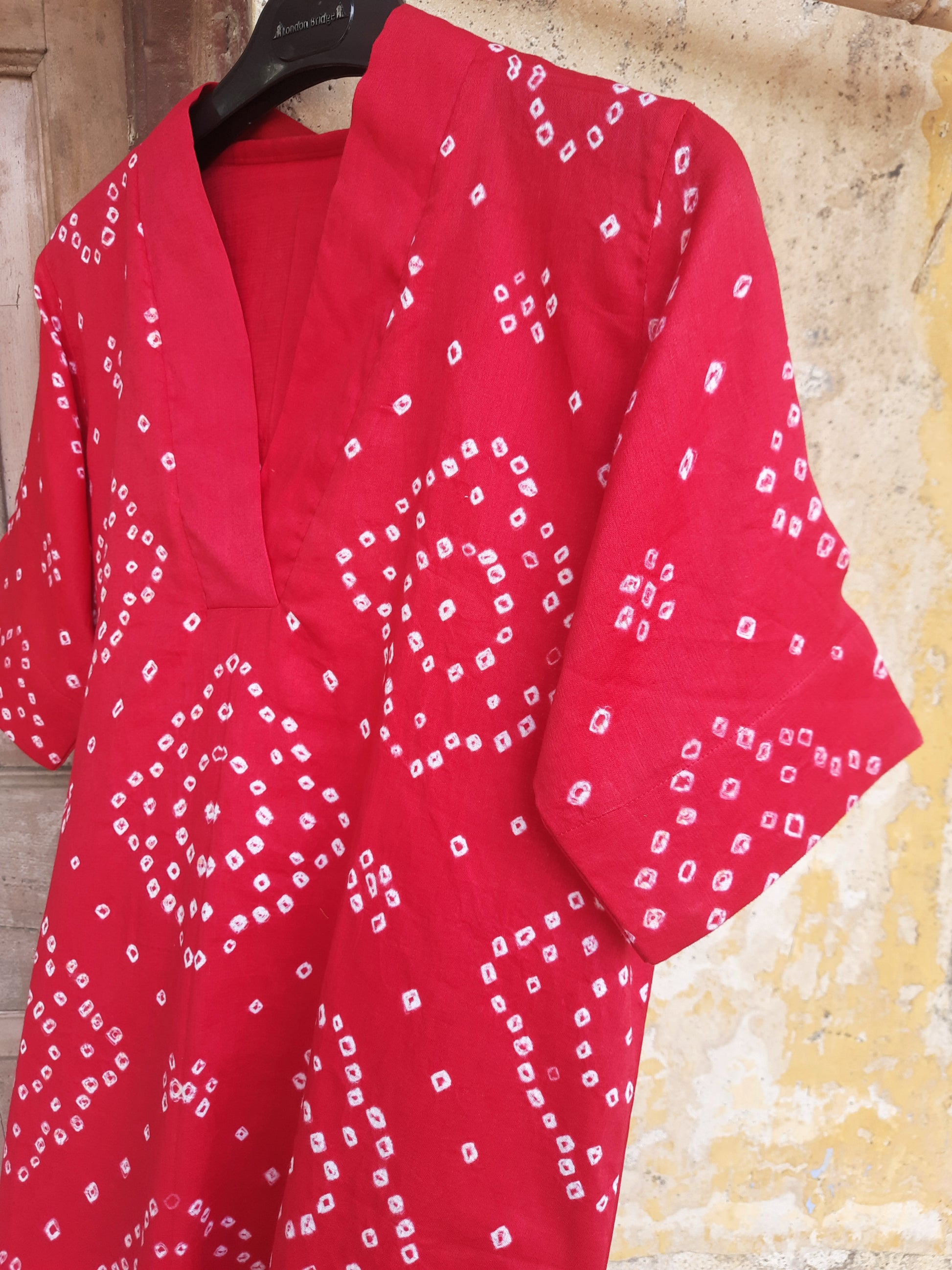 A deep pink, handcrafted cotton satin bandhani oversized top for women. This comfortable, loose-fit designer top features a traditional hand tie-dyed pattern, short side slits, and a V-neckline, perfect for casual or everyday ethnic wear. Ideal for a modern, relaxed style.