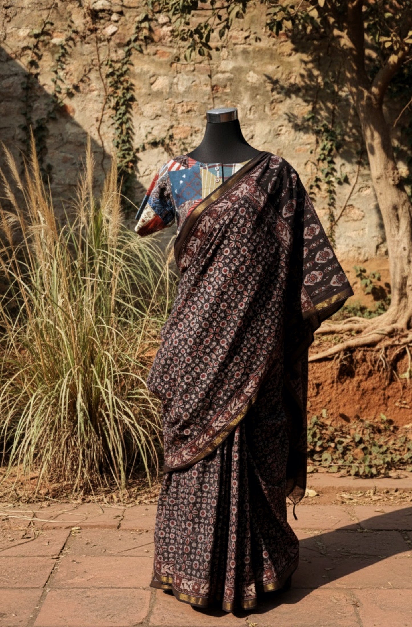 Black Ajrakh hand block printed pure cotton saree featuring traditional natural-dyed motifs and detailed Ajrakh border. Slow made, handmade saree measuring 6.30 meters with a 44-inch width. Styled with a patchwork blouse.