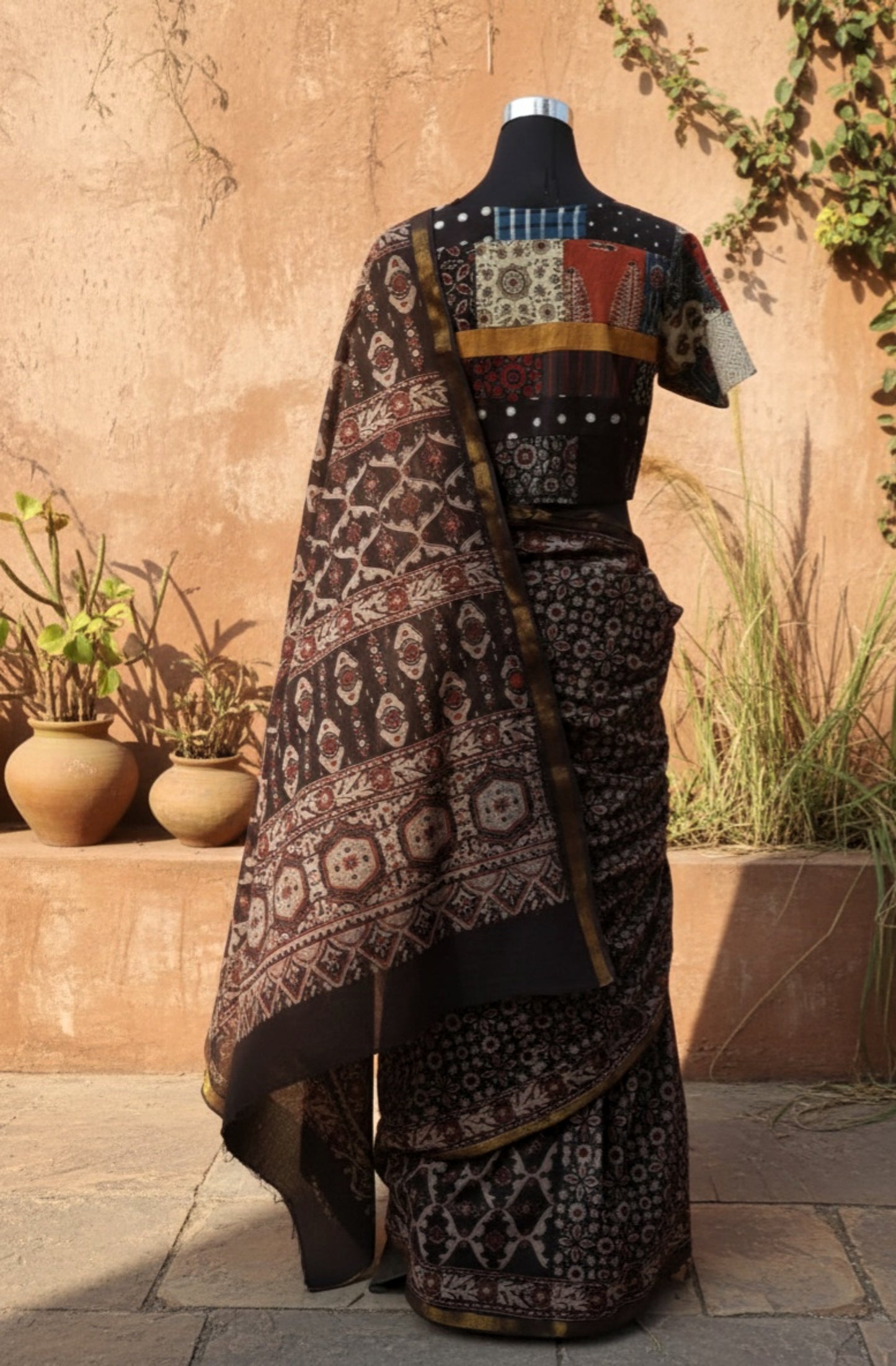 Black Ajrakh hand block printed pure cotton saree featuring traditional natural-dyed motifs and detailed Ajrakh border. Slow made, handmade saree measuring 6.30 meters with a 44-inch width. Styled with a patchwork blouse.