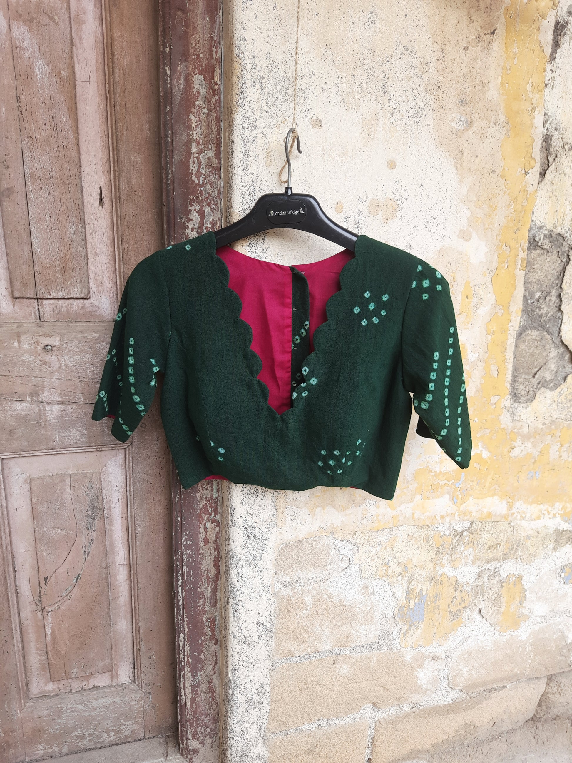 Handcrafted green Bandhani tie-dye blouse made from hand-spun and handwoven organic cotton, featuring a scalloped deep V-neck, pink lining, padded design, and back button closure - festive, elegant, and eco-conscious.