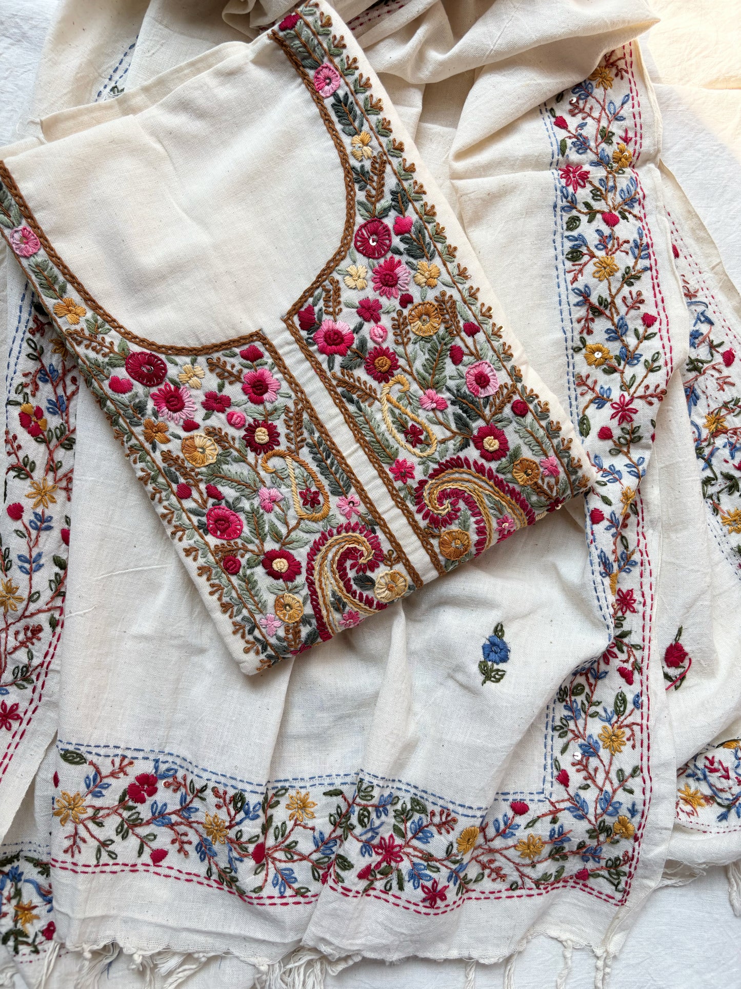 Handspun cotton unstitched kurta dupatta set featuring a richly hand embroidered paisley and floral yoke in warm pink, mustard, blue, and earthy tones, paired with a hand embroidered dupatta with floral vine borders and tassel edges.