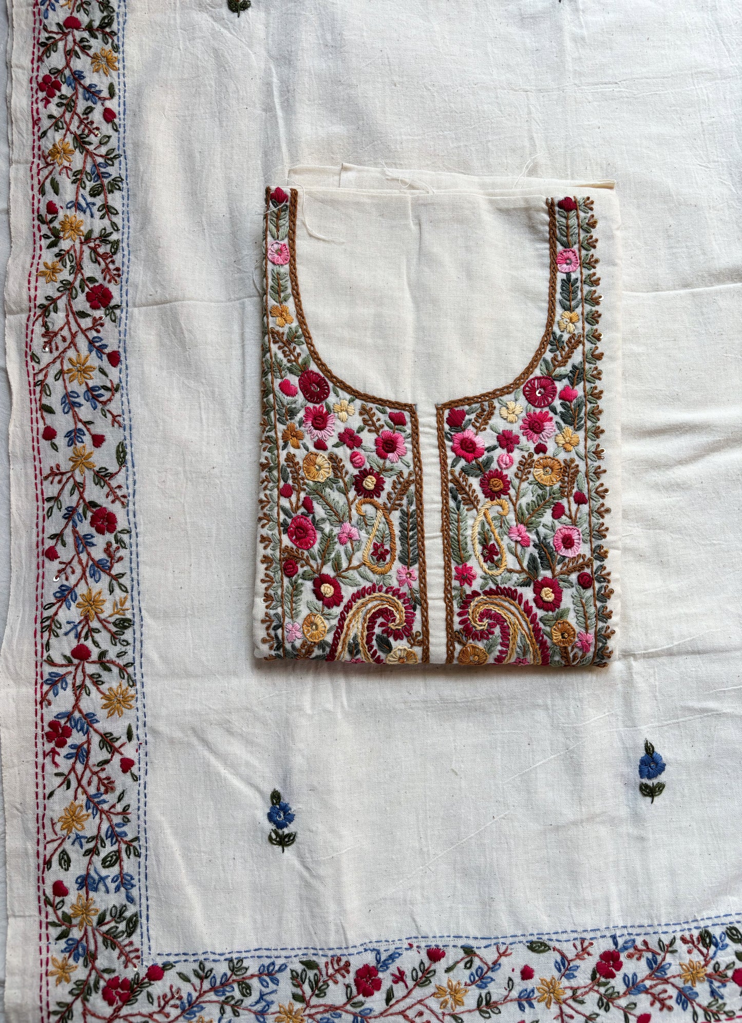 Handspun cotton unstitched kurta dupatta set featuring a richly hand embroidered paisley and floral yoke in warm pink, mustard, blue, and earthy tones, paired with a hand embroidered dupatta with floral vine borders and tassel edges.