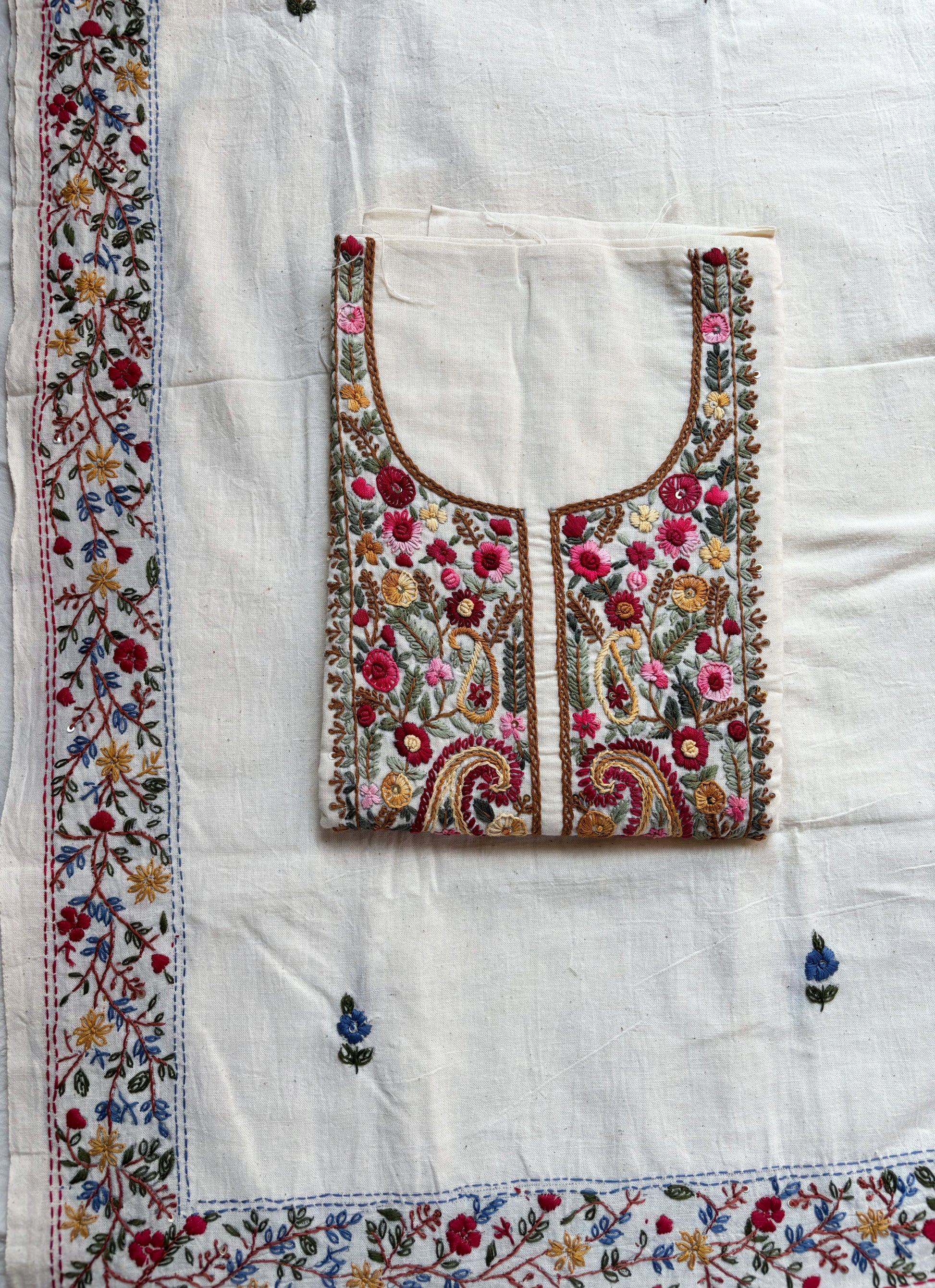 Handspun cotton unstitched kurta dupatta set featuring a richly hand embroidered paisley and floral yoke in warm pink, mustard, blue, and earthy tones, paired with a hand embroidered dupatta with floral vine borders and tassel edges.