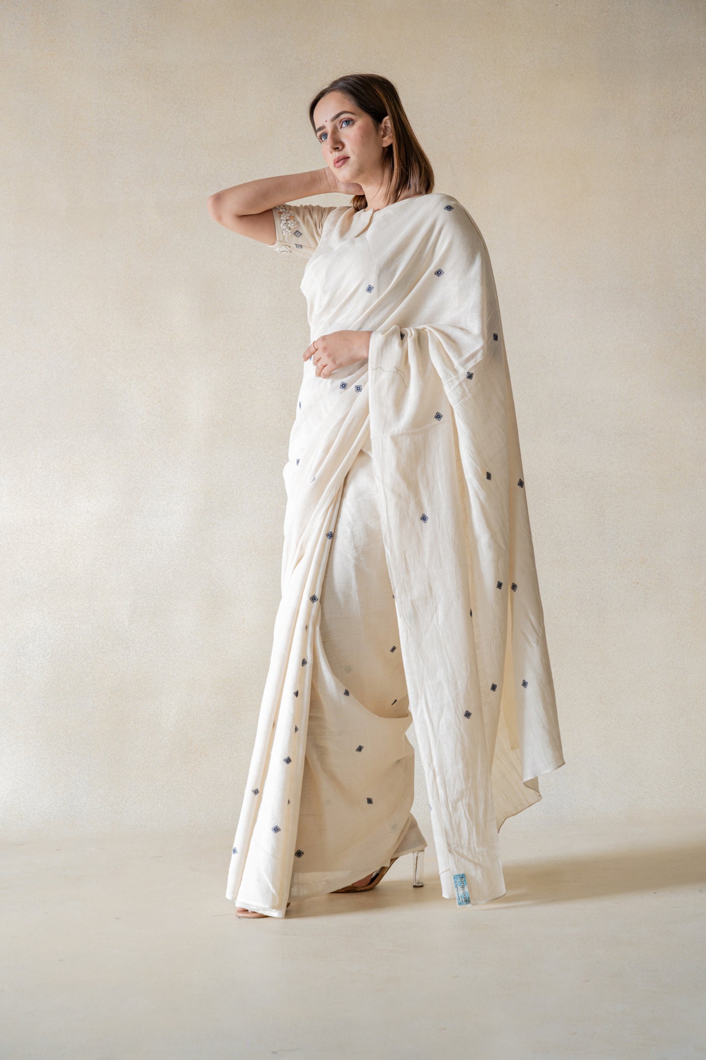 Off-white handspun and handwoven organic cotton saree crafted by artisans in Gujarat, slow-made Indian wear, minimal embroidered motifs, authentic handmade saree draped on model.