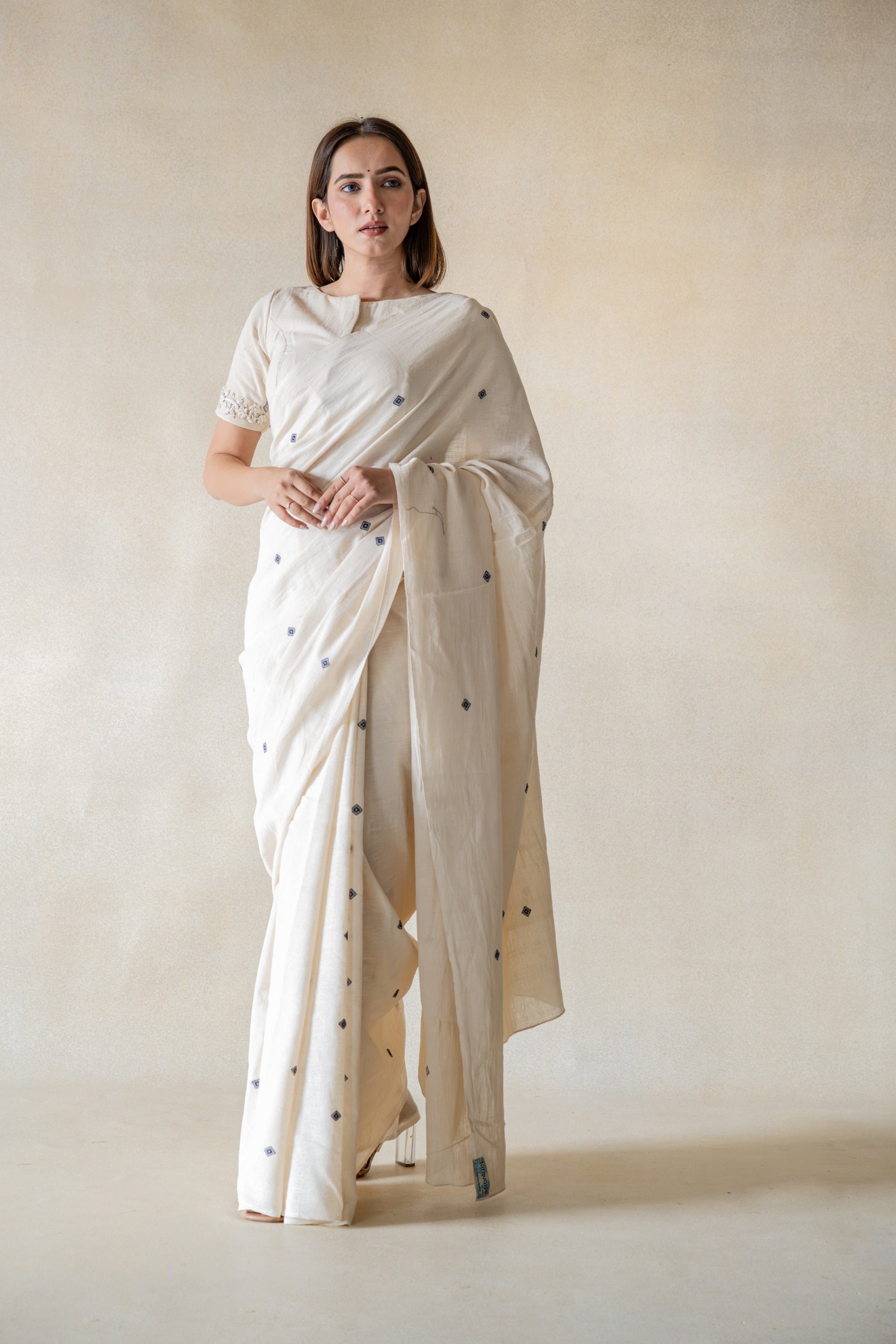 Off-white handspun and handwoven organic cotton saree crafted by artisans in Gujarat, slow-made Indian wear, minimal embroidered motifs, authentic handmade saree draped on model.