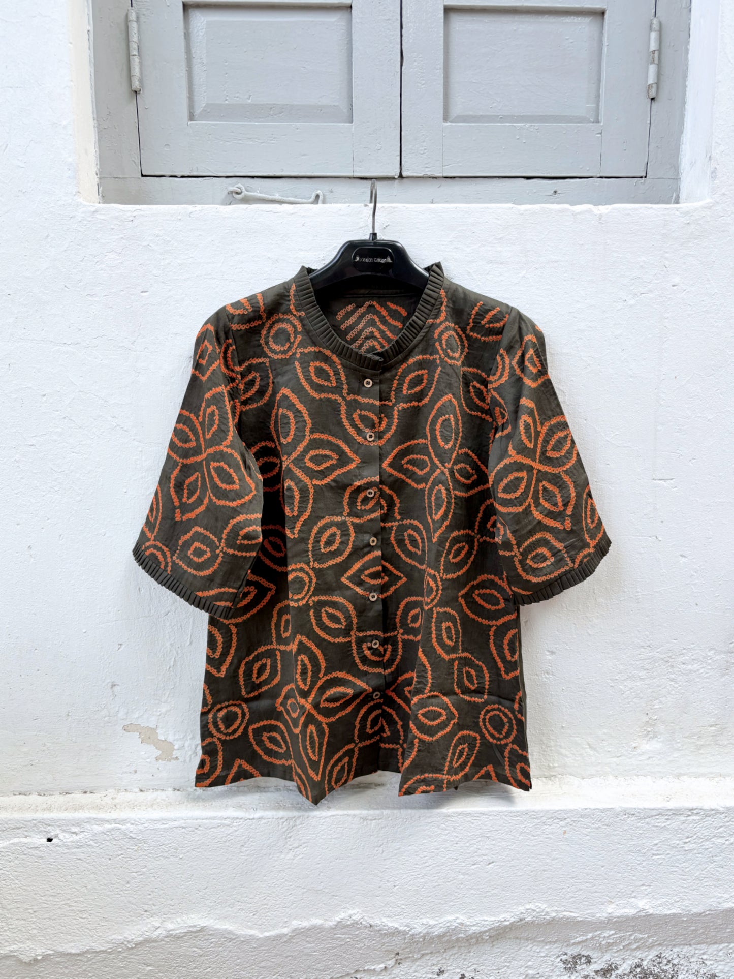Jhankar Bandhani cotton shirt in smoky charcoal grey with burnt rust orange floral motifs, pleated neckline, pleated sleeve hems, coconut shell buttons, and relaxed fit.