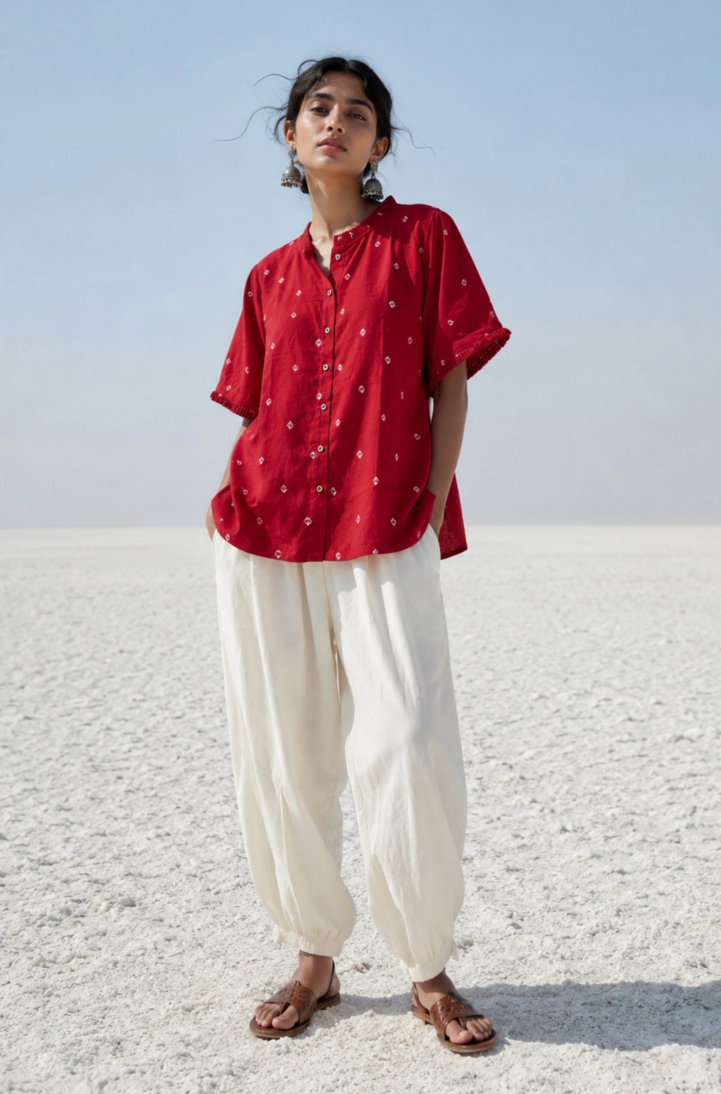 Red cotton satin Bandhani shirt with hand tie-dyed white motifs, pleated round neckline, pleated sleeve hems, coconut shell button closure, relaxed fit, and short side slits. Features Bandhani detailing on both the front and back.