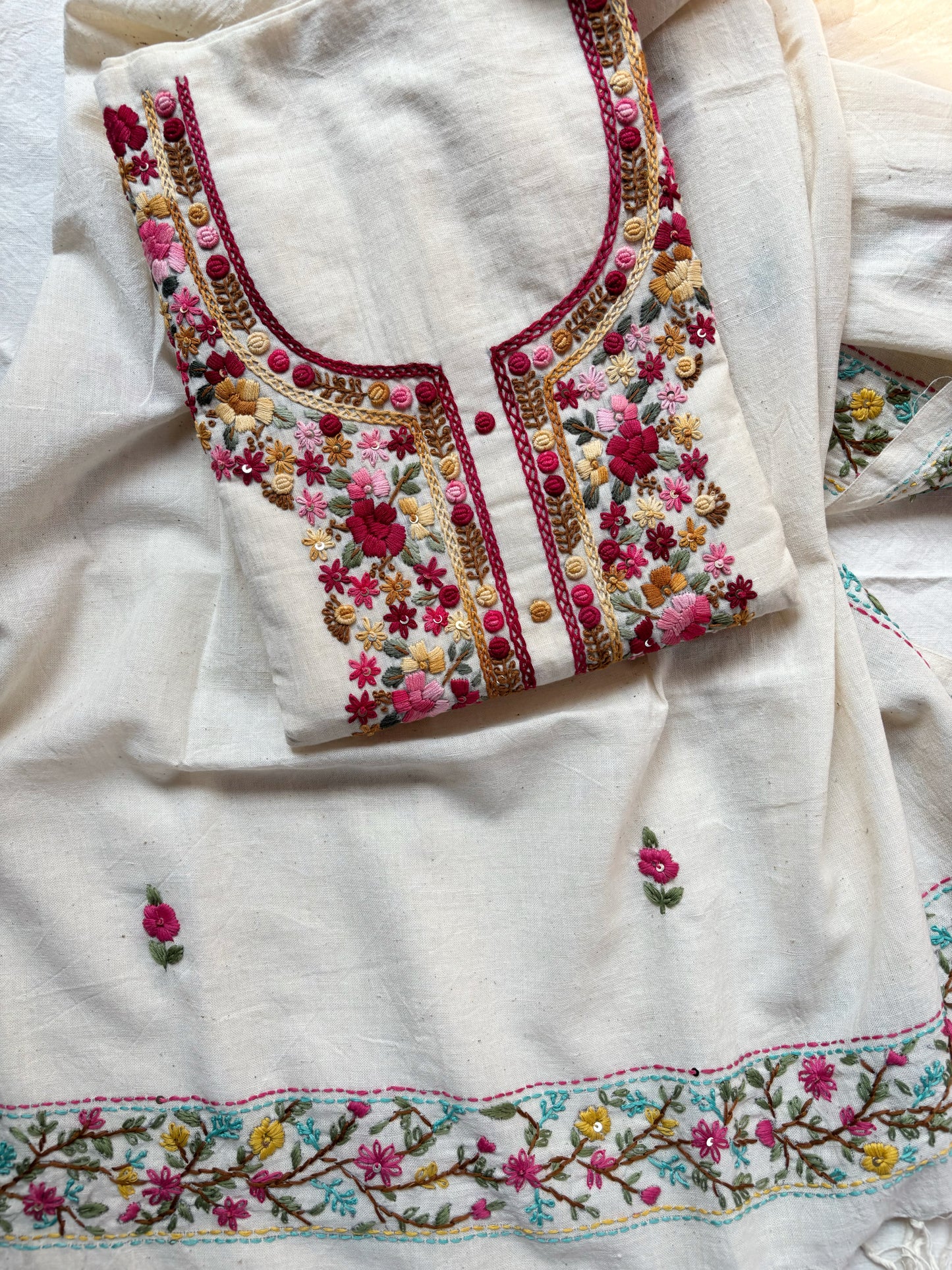 Handspun cotton unstitched kurta dupatta set featuring a floral hand embroidered yoke in pink and earthy tones, small butti motifs on the kurta, and a matching hand embroidered dupatta with tassels.