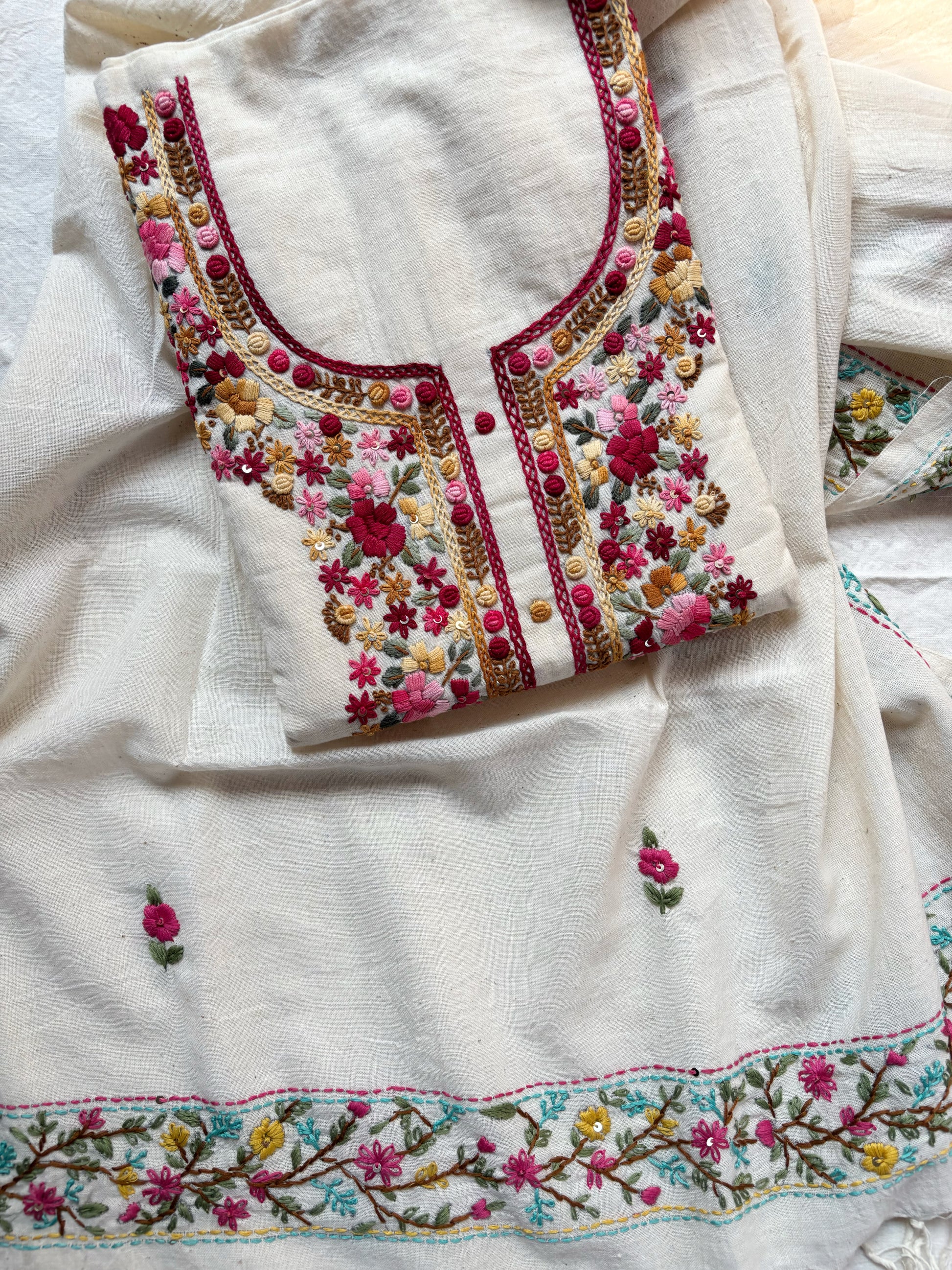 Handspun cotton unstitched kurta dupatta set featuring a floral hand embroidered yoke in pink and earthy tones, small butti motifs on the kurta, and a matching hand embroidered dupatta with tassels.