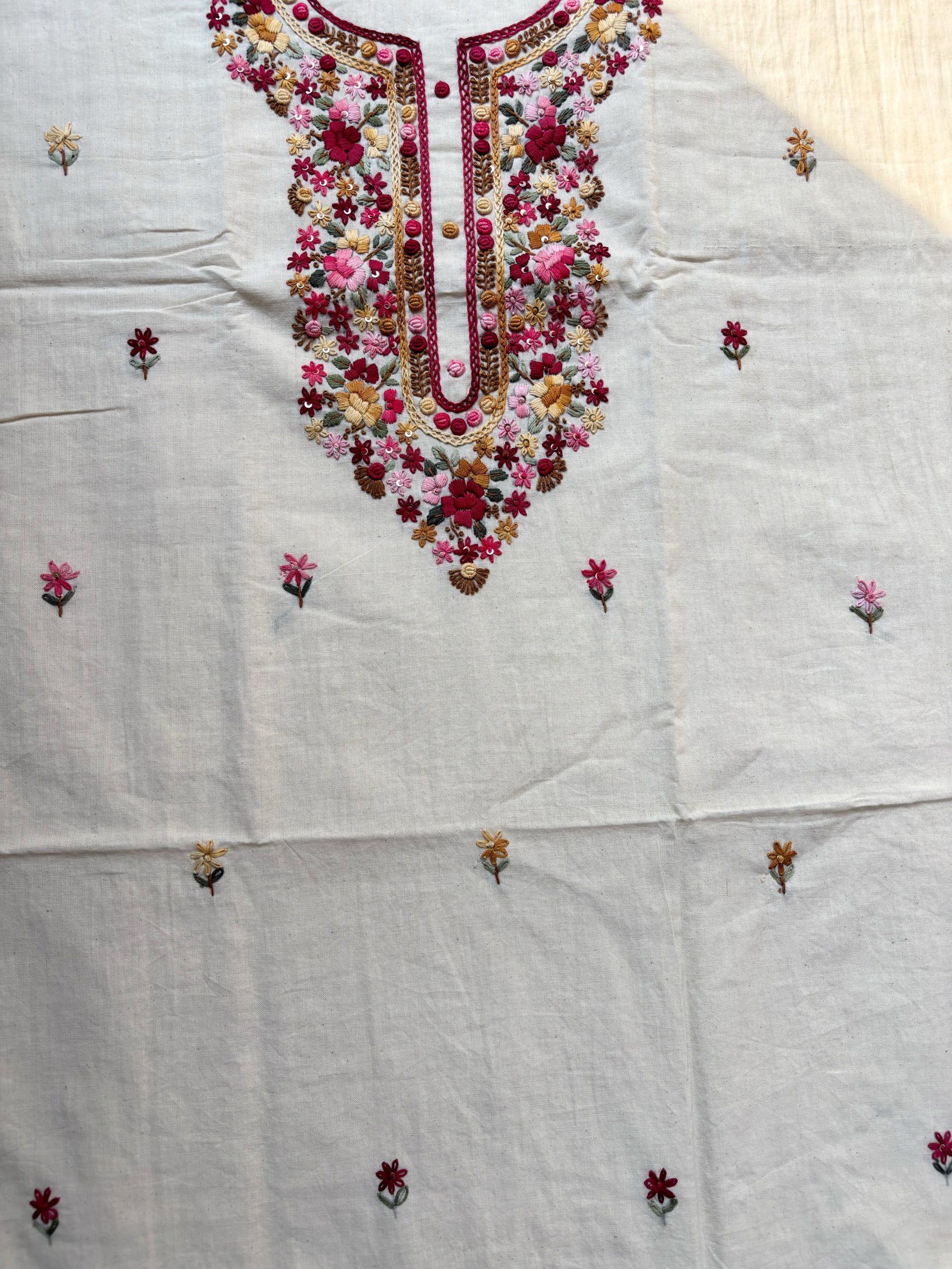 Handspun cotton unstitched kurta dupatta set featuring a floral hand embroidered yoke in pink and earthy tones, small butti motifs on the kurta, and a matching hand embroidered dupatta with tassels.