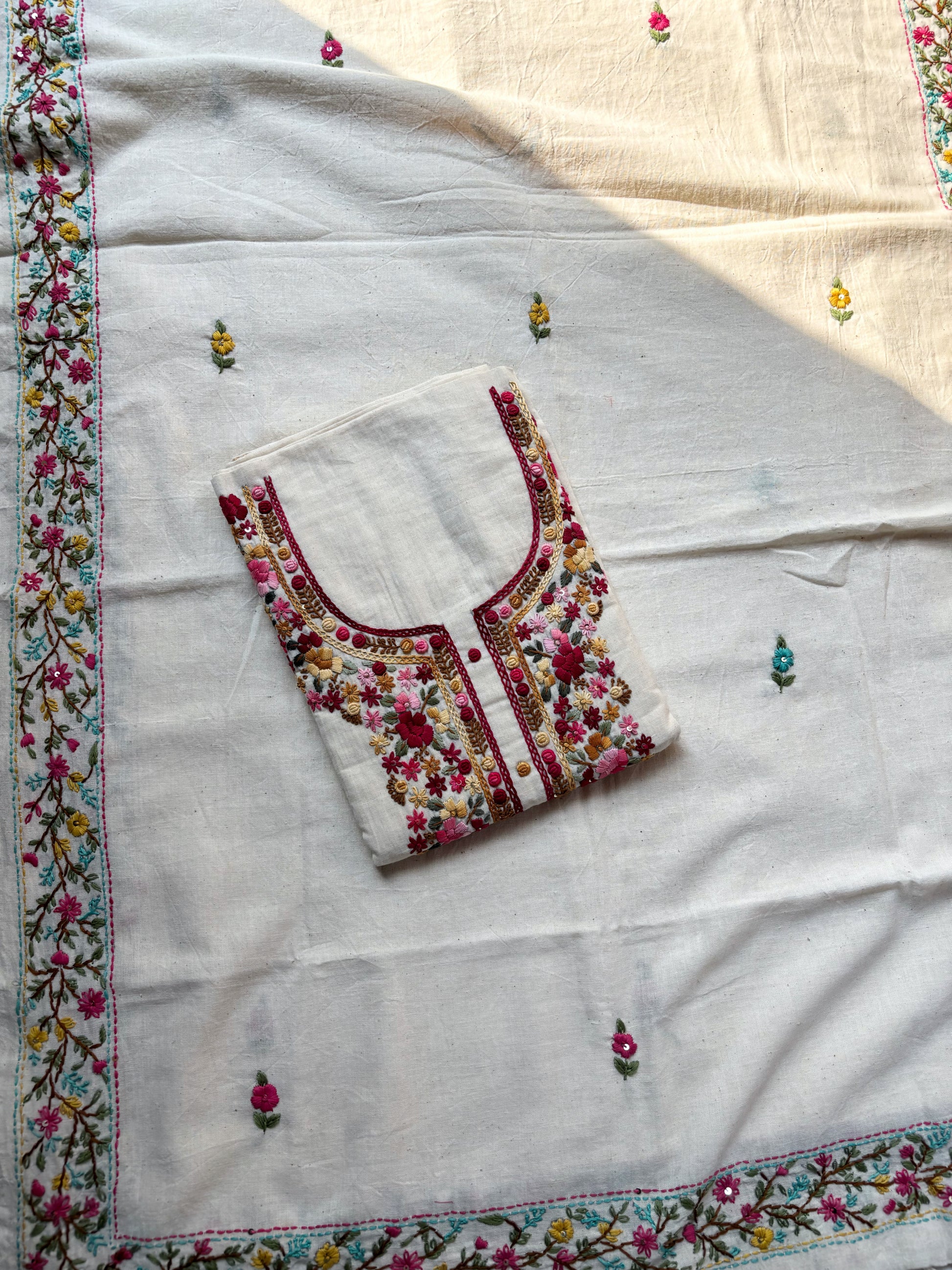 Handspun cotton unstitched kurta dupatta set featuring a floral hand embroidered yoke in pink and earthy tones, small butti motifs on the kurta, and a matching hand embroidered dupatta with tassels.