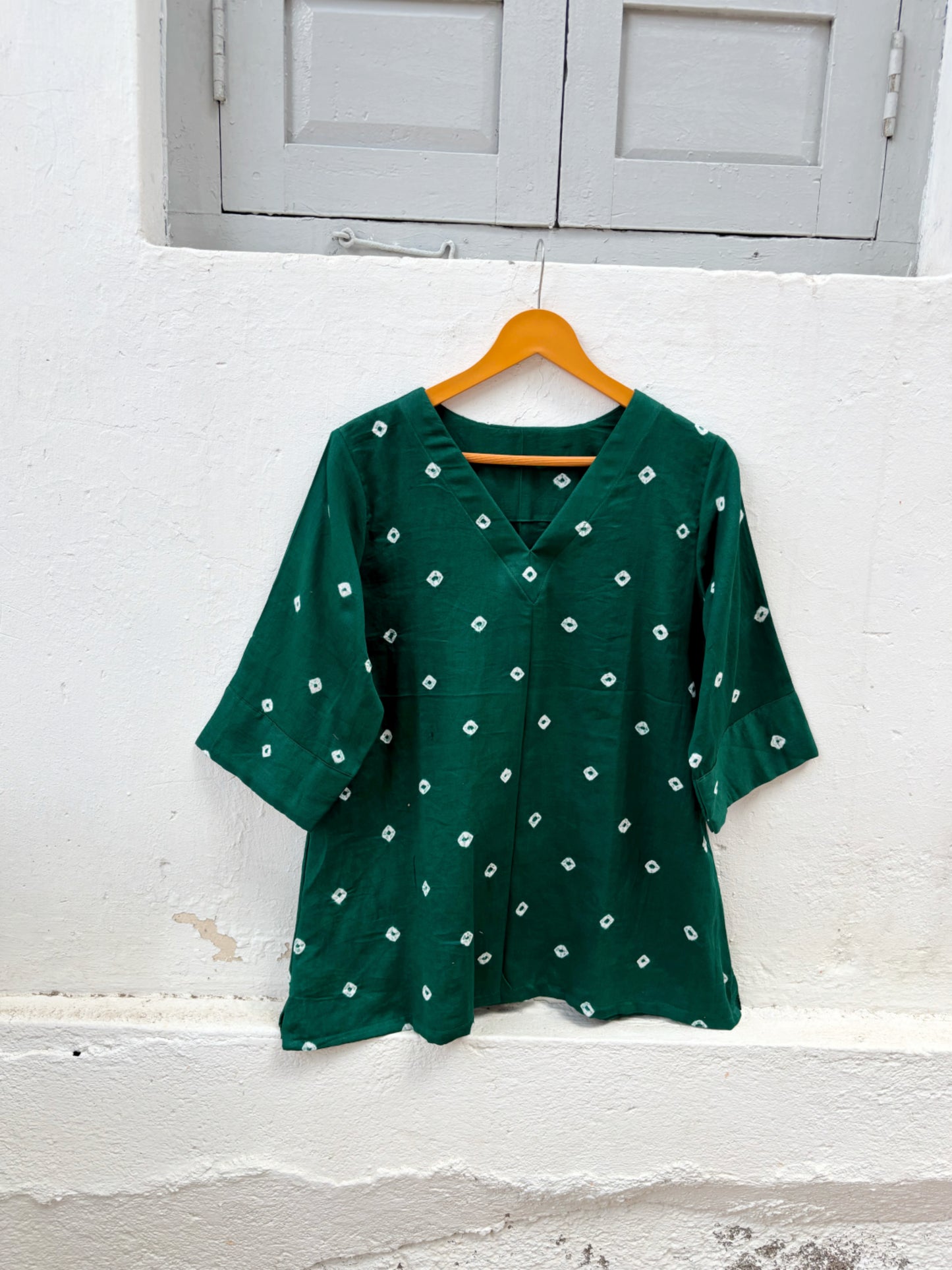 Emerald green cotton satin Bandhani top with hand tie-dyed white motifs, V-neckline, elbow-length sleeves, relaxed fit, and scattered Bandhani pattern.