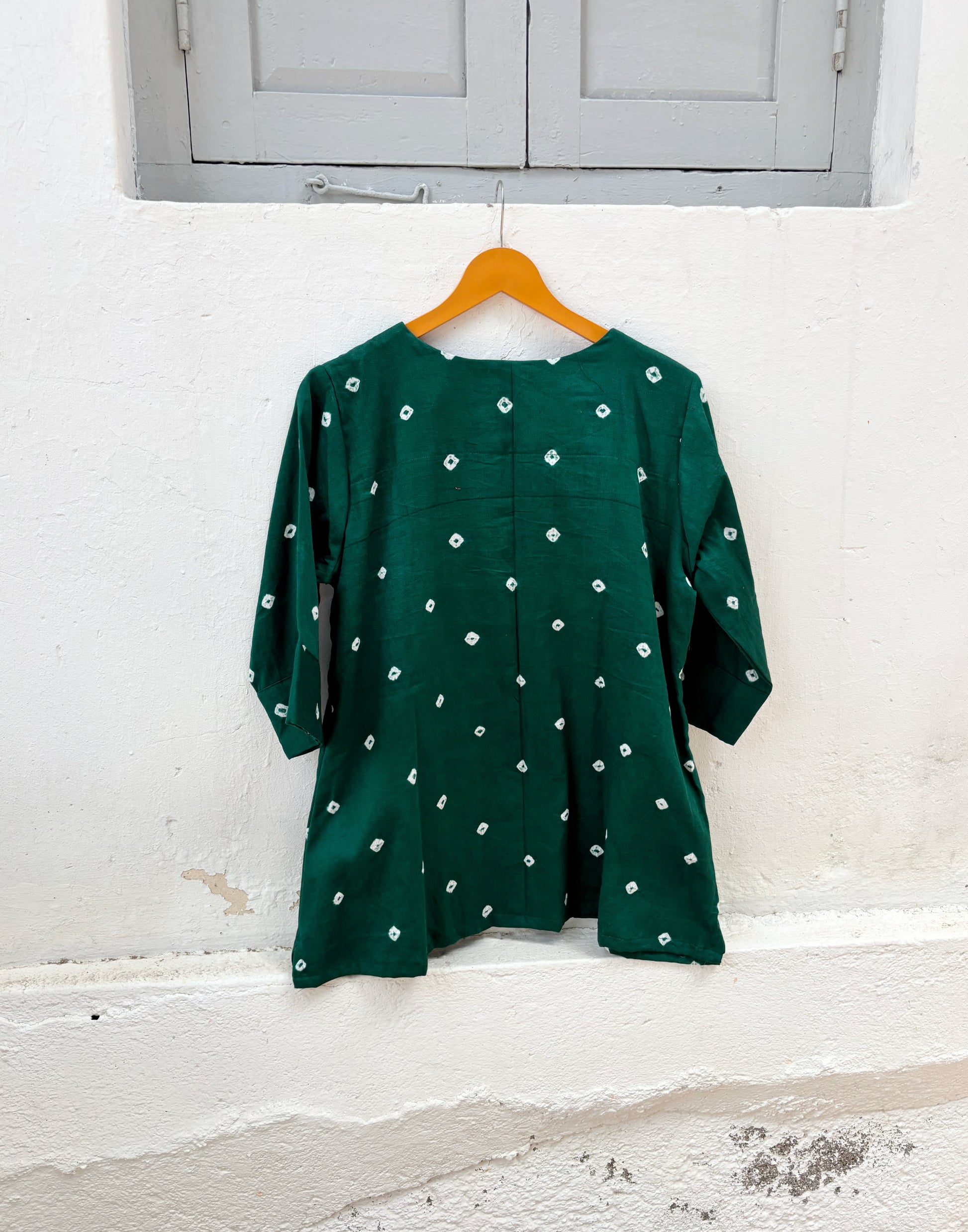 Emerald green cotton satin Bandhani top with hand tie-dyed white motifs, V-neckline, elbow-length sleeves, relaxed fit, and scattered Bandhani pattern.
