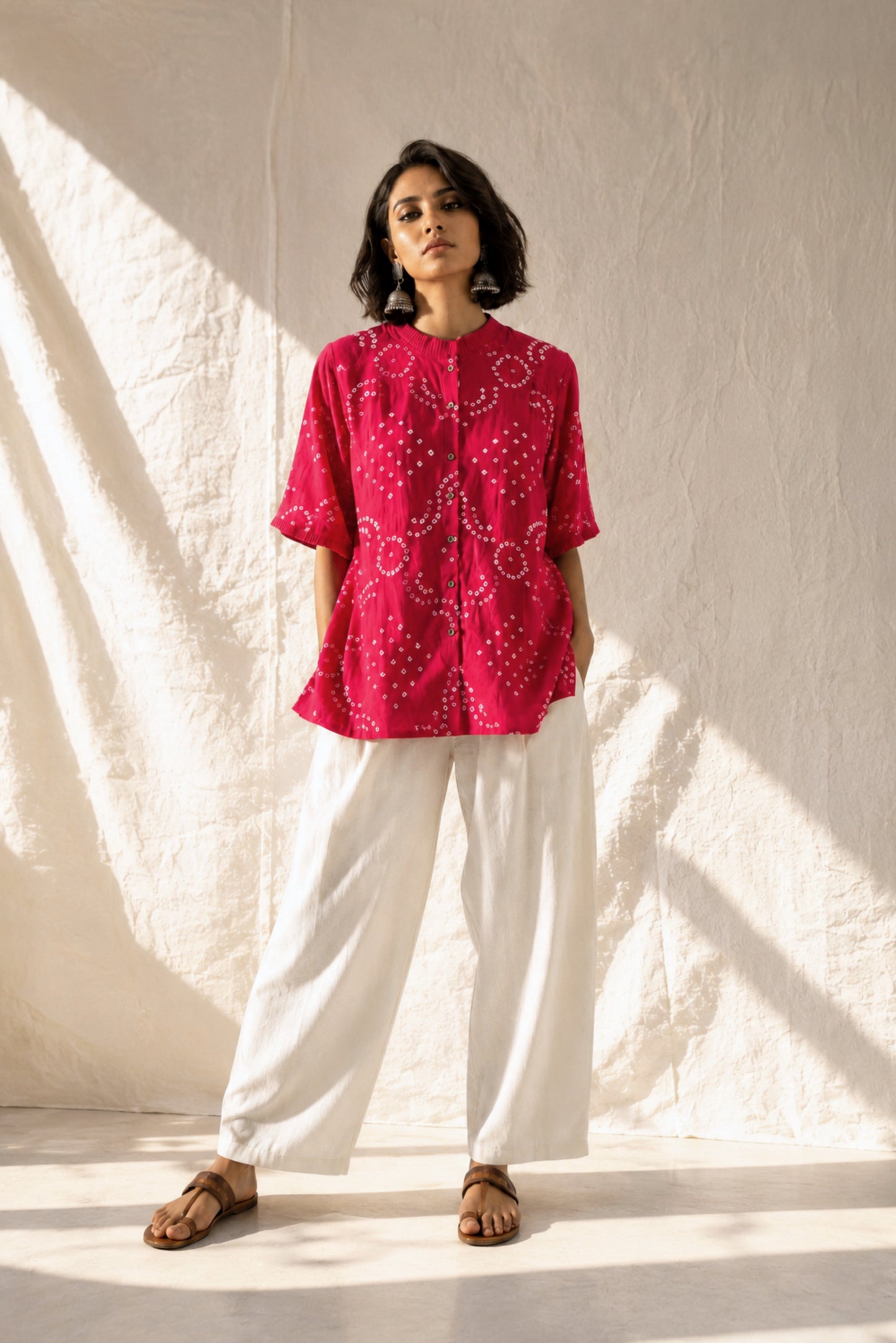 Hand tie-dyed Gulnaar Bandhani cotton satin shirt in deep bougainvillea pink with pleated neckline, pleated sleeve hems and handcrafted Bandhani motifs.