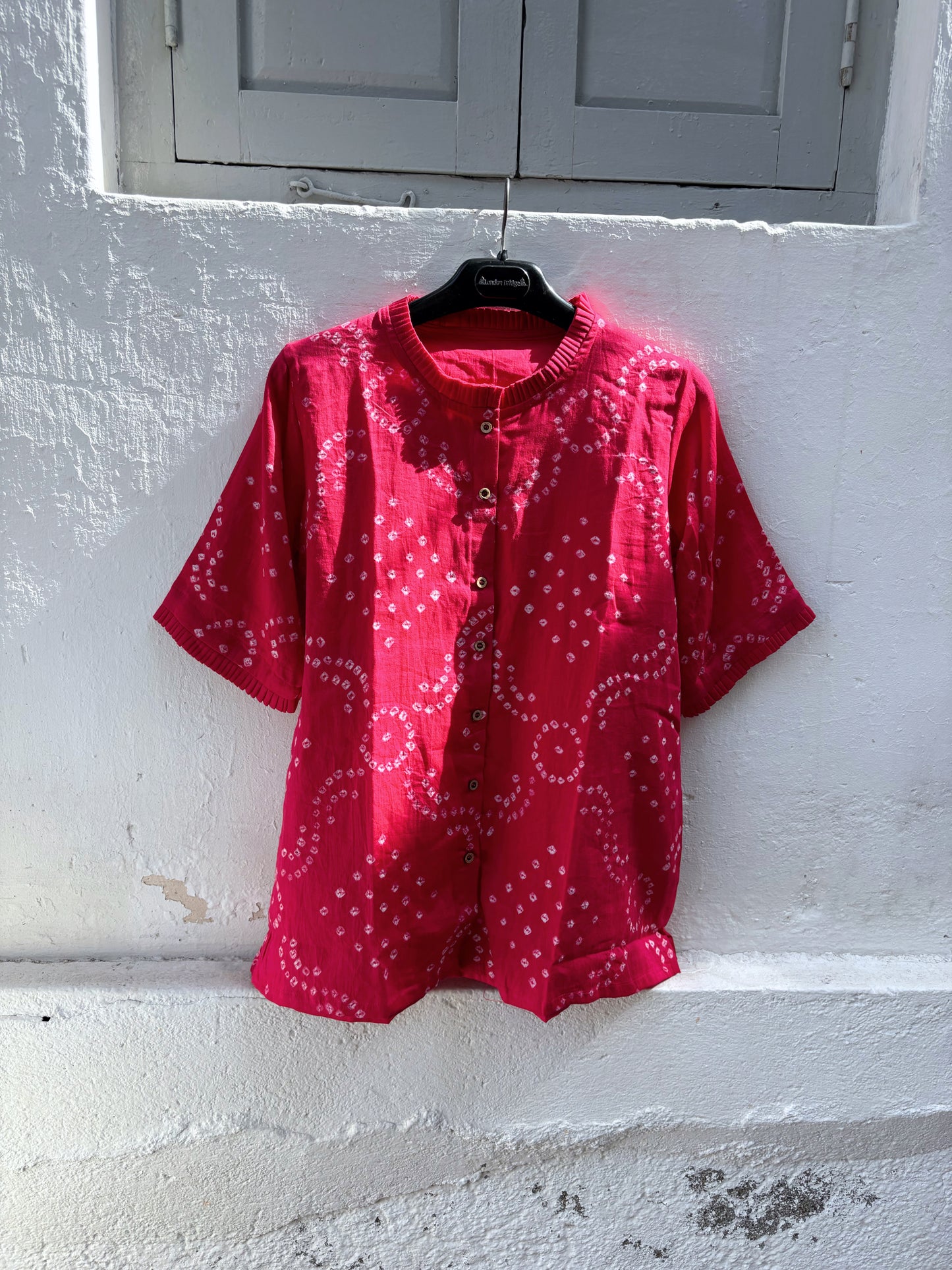 Hand tie-dyed Gulnaar Bandhani cotton satin shirt in deep bougainvillea pink with pleated neckline, pleated sleeve hems and handcrafted Bandhani motifs.

