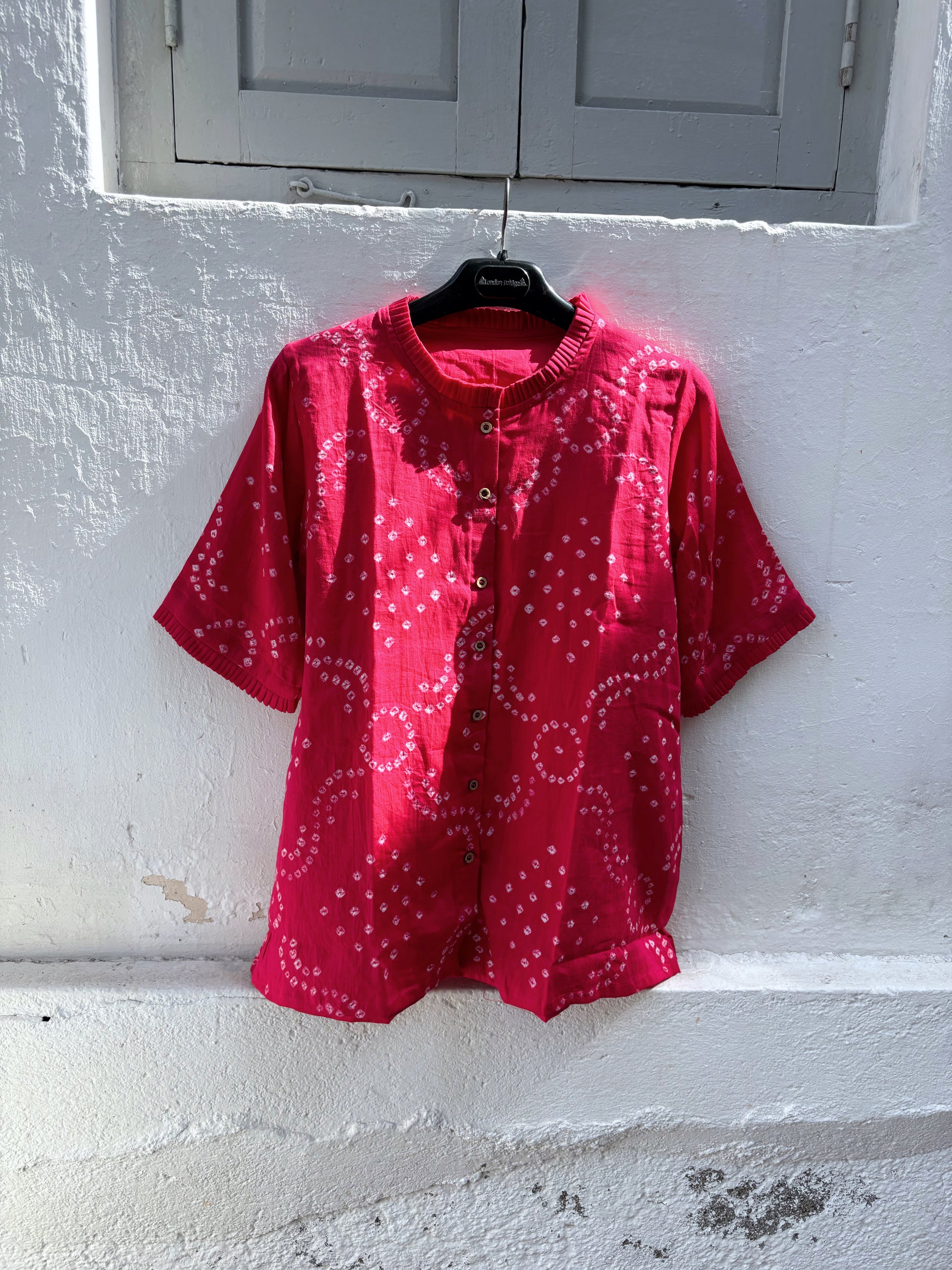 Hand tie-dyed Gulnaar Bandhani cotton satin shirt in deep bougainvillea pink with pleated neckline, pleated sleeve hems and handcrafted Bandhani motifs.
