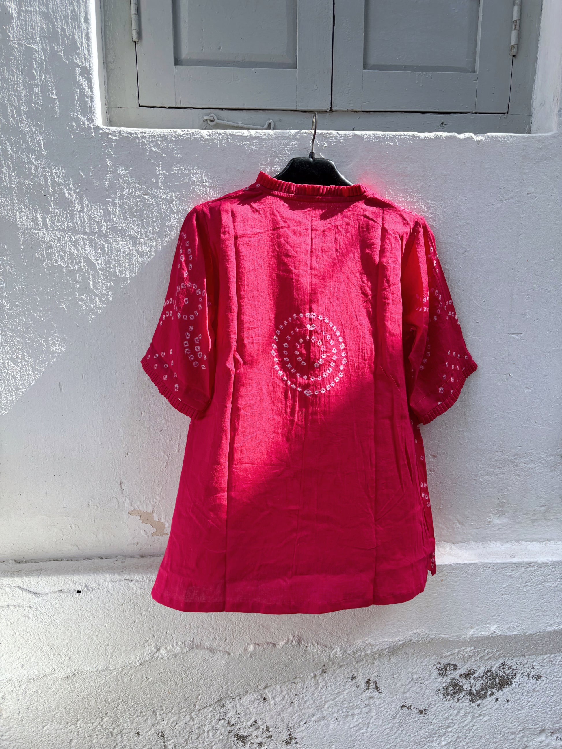 Hand tie-dyed Gulnaar Bandhani cotton satin shirt in deep bougainvillea pink with pleated neckline, pleated sleeve hems and handcrafted Bandhani motifs.
