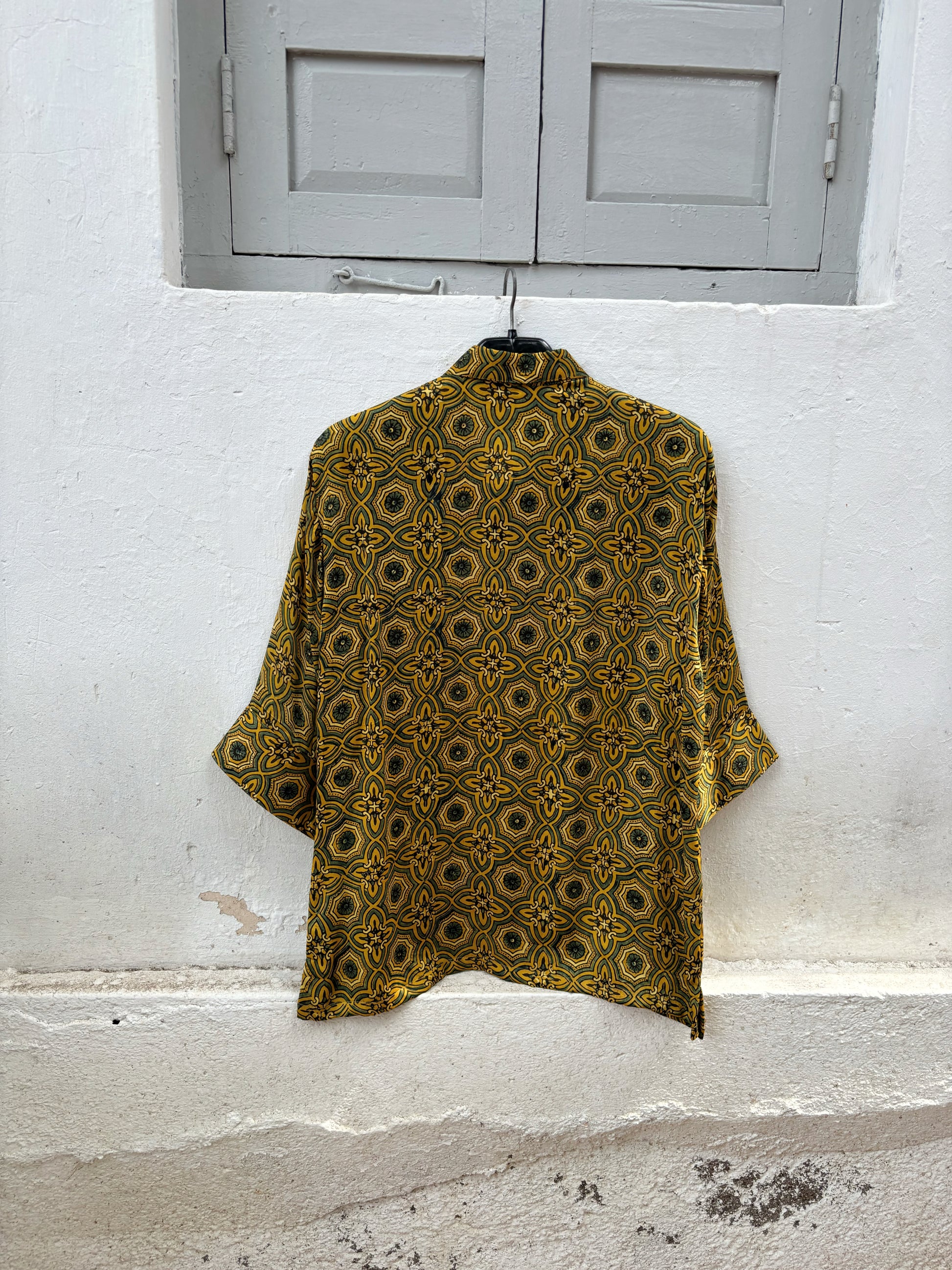 Turmeric dyed Ajrakh hand block printed modal silk oversized shirt for women in golden yellow with olive green and iron black geometric motifs.
