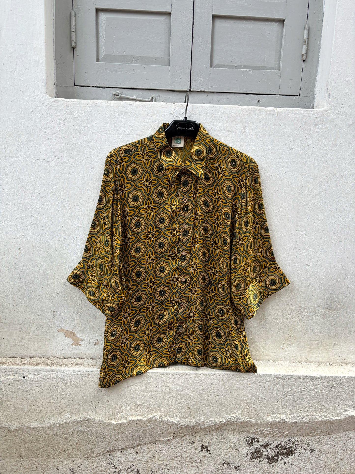Turmeric dyed Ajrakh hand block printed modal silk oversized shirt for women in golden yellow with olive green and iron black geometric motifs.
