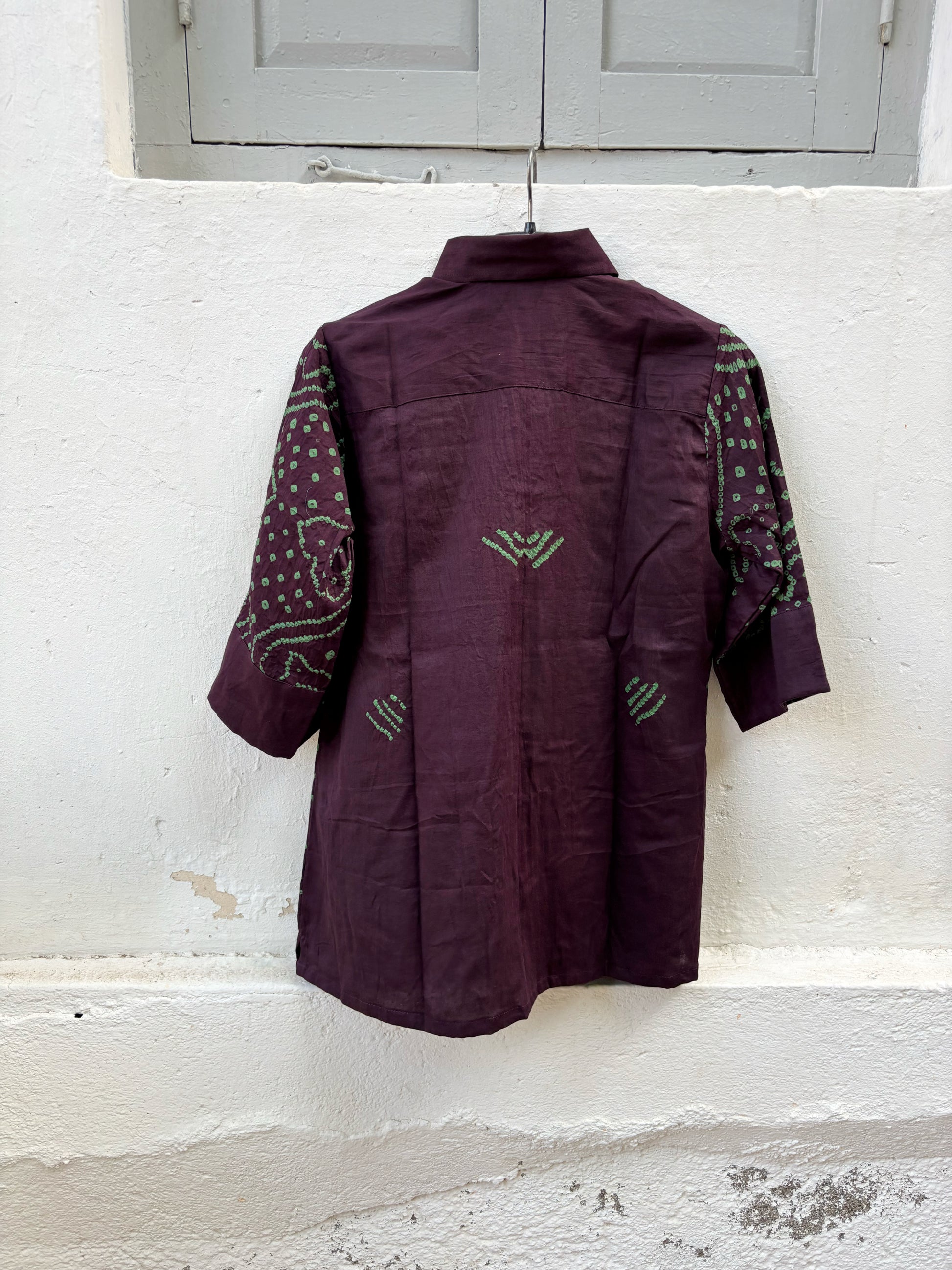 Jhankar Bandhani cotton shirt in deep jamun purple with sage green paisley motifs, classic shirt collar, folded sleeve cuffs, coconut shell buttons, and relaxed fit.