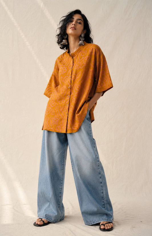 Hand tie-dyed Kesari ochre cotton Bandhani shirt with muted purple Jhankaar motifs, pleated neckline and relaxed fit.