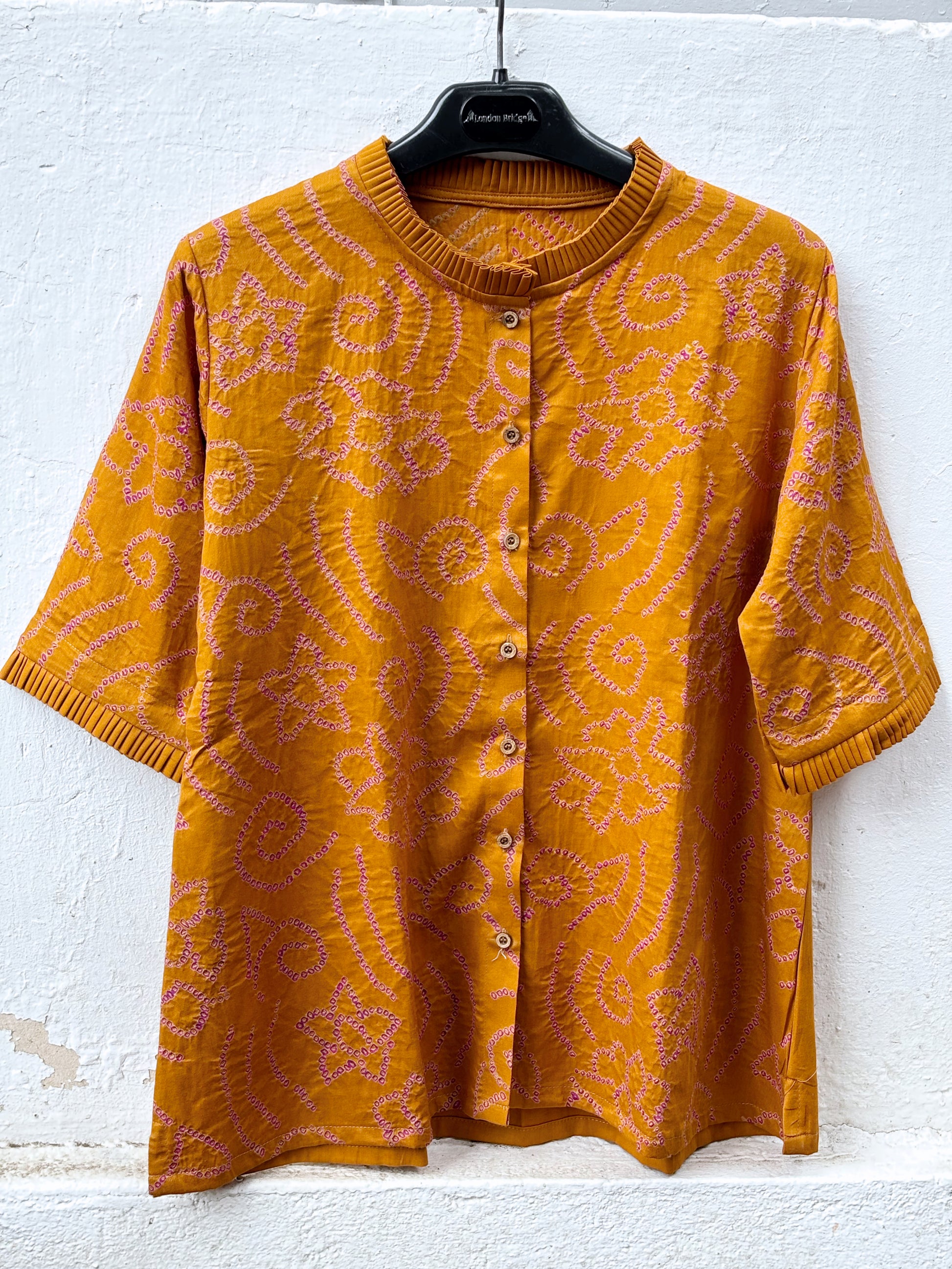 Hand tie-dyed Kesari ochre cotton Bandhani shirt with muted purple Jhankaar motifs, pleated neckline and relaxed fit.