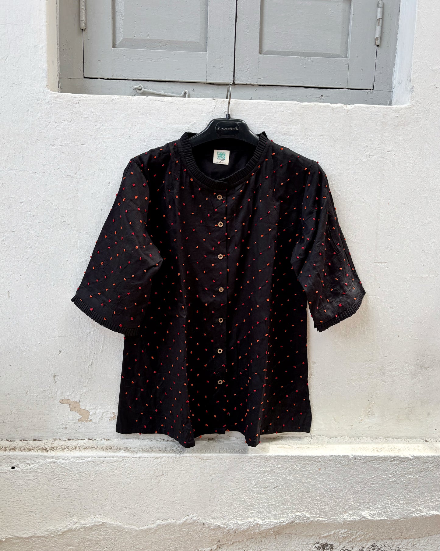 Black cotton satin shirt with burnt orange and deep red hand-tied thread knot detailing, pleated neckline and plain black back.