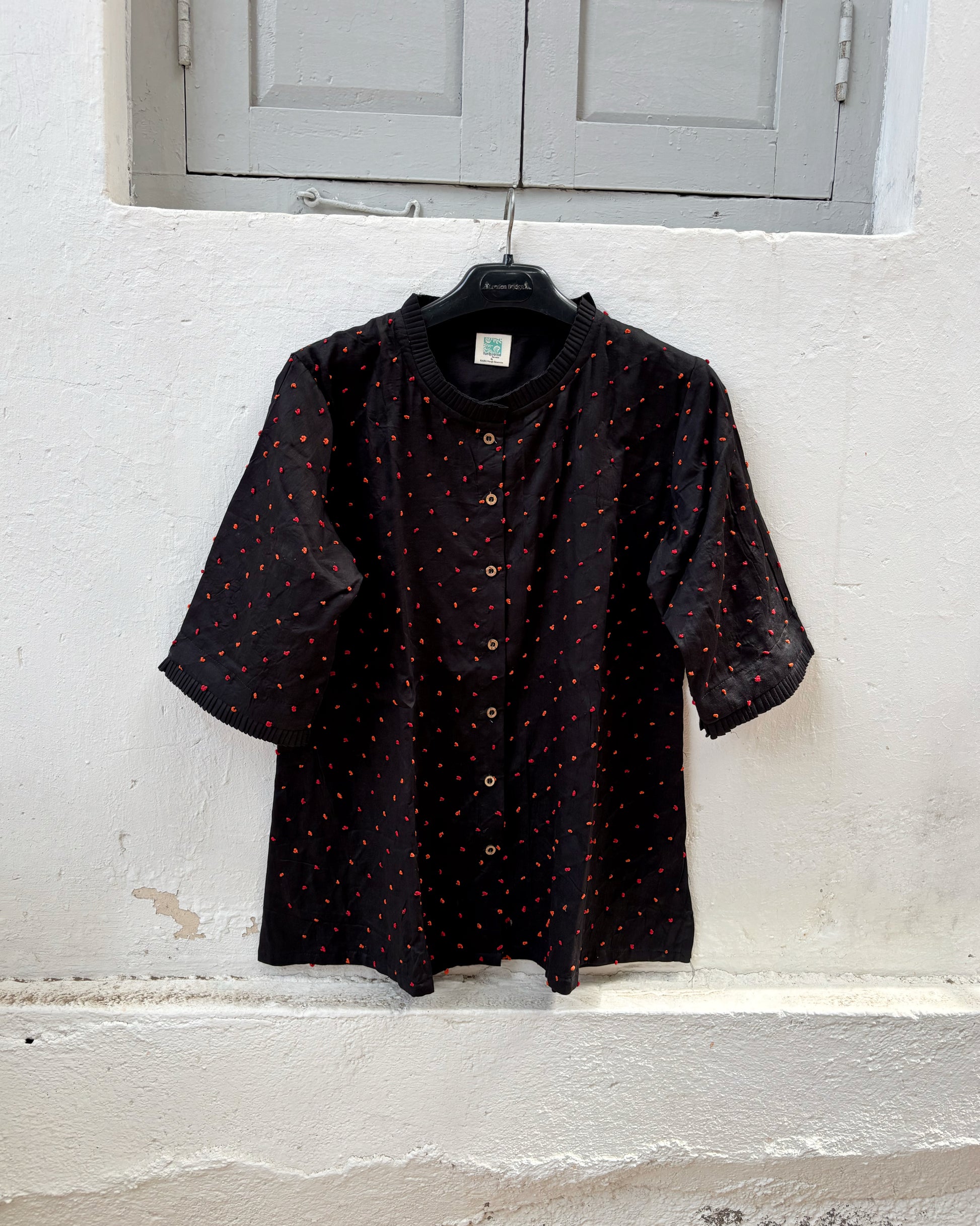 Black cotton satin shirt with burnt orange and deep red hand-tied thread knot detailing, pleated neckline and plain black back.