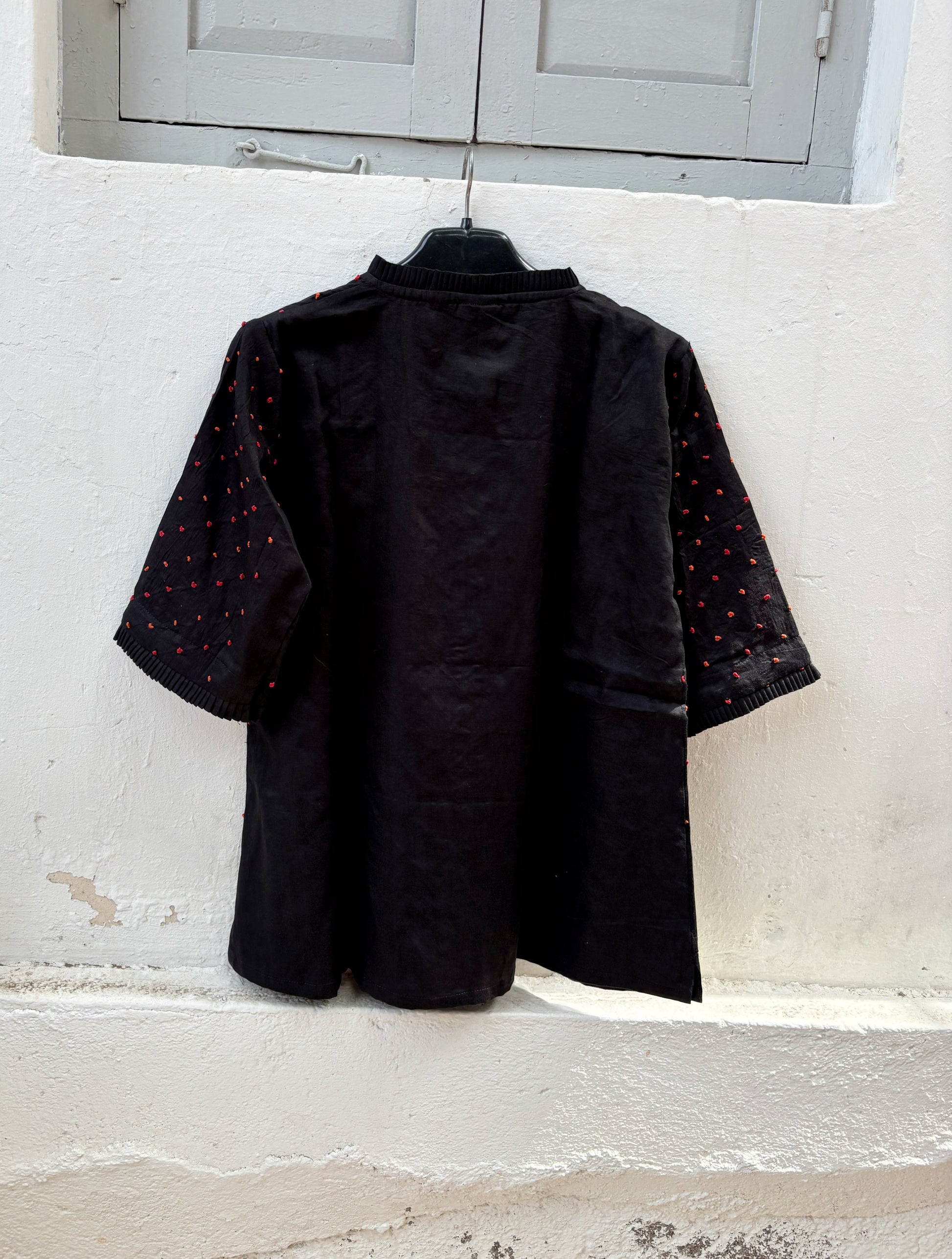 Black cotton satin shirt with burnt orange and deep red hand-tied thread knot detailing, pleated neckline and plain black back.