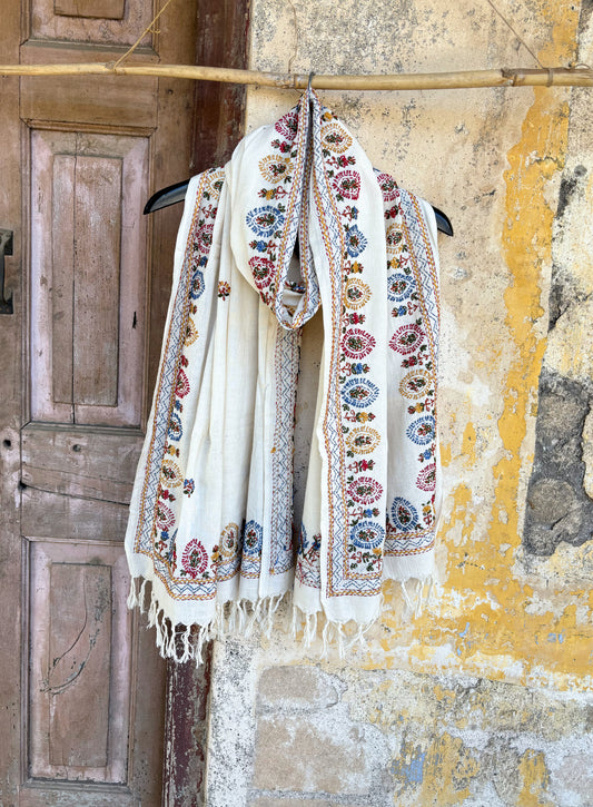 Handspun cotton dupatta in warm ivory shade featuring repeated floral hand embroidered motifs in red, blue, mustard, and green. Lightweight handcrafted dupatta with tassel edges, named Kalika.
