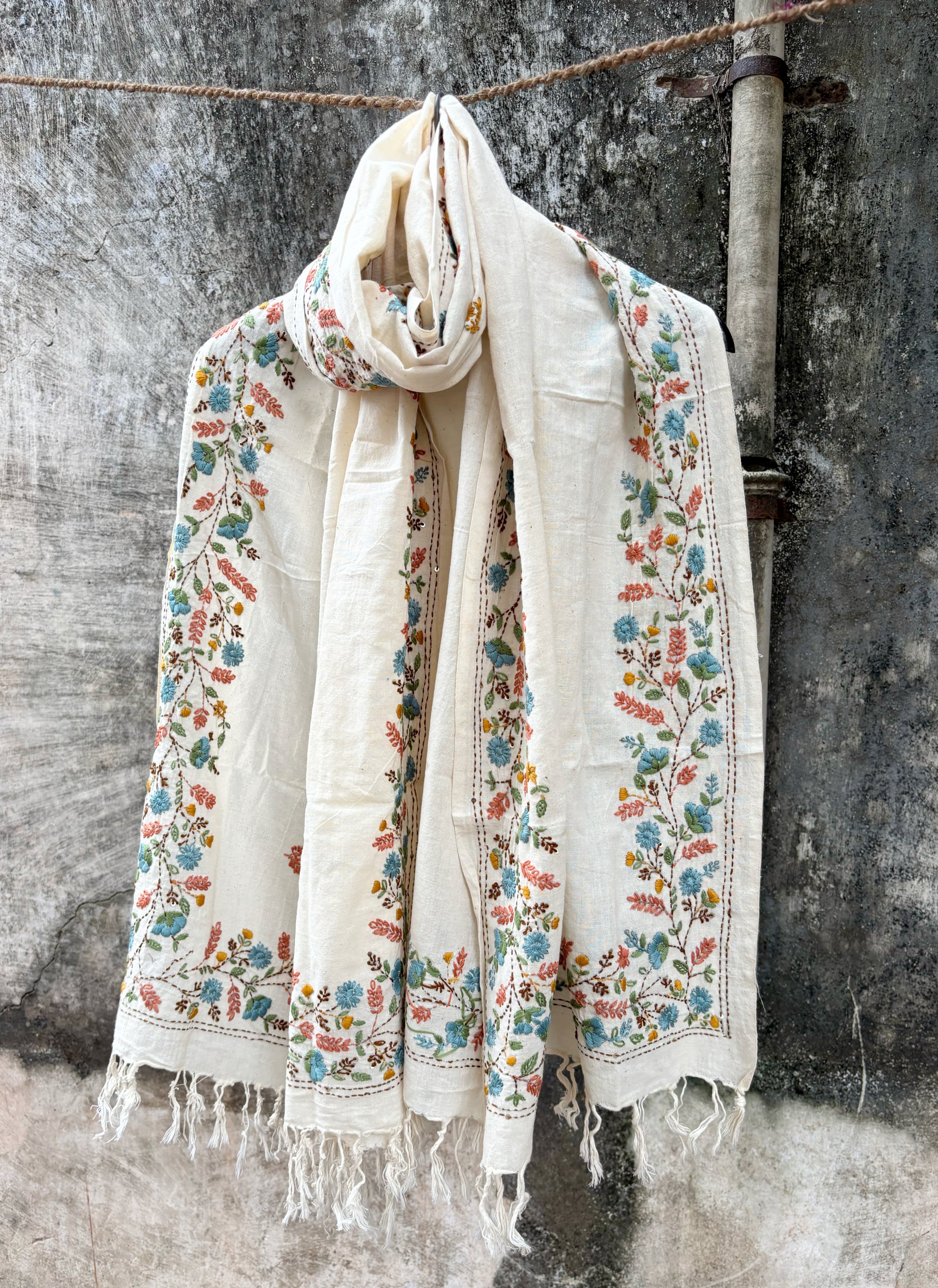 Maalti hand spun and handwoven off-white cotton dupatta with powder blue, coral, mustard, and olive floral embroidered borders, scattered floral butis, and handcrafted tassels.
