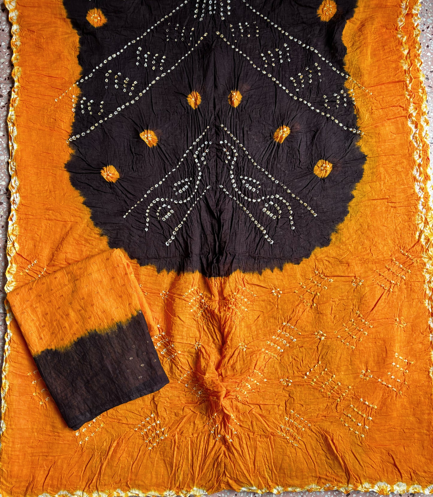 Marigold and deep brown hand tie-dyed Bandhani cotton saree with traditional dotted motifs and geometric border.
