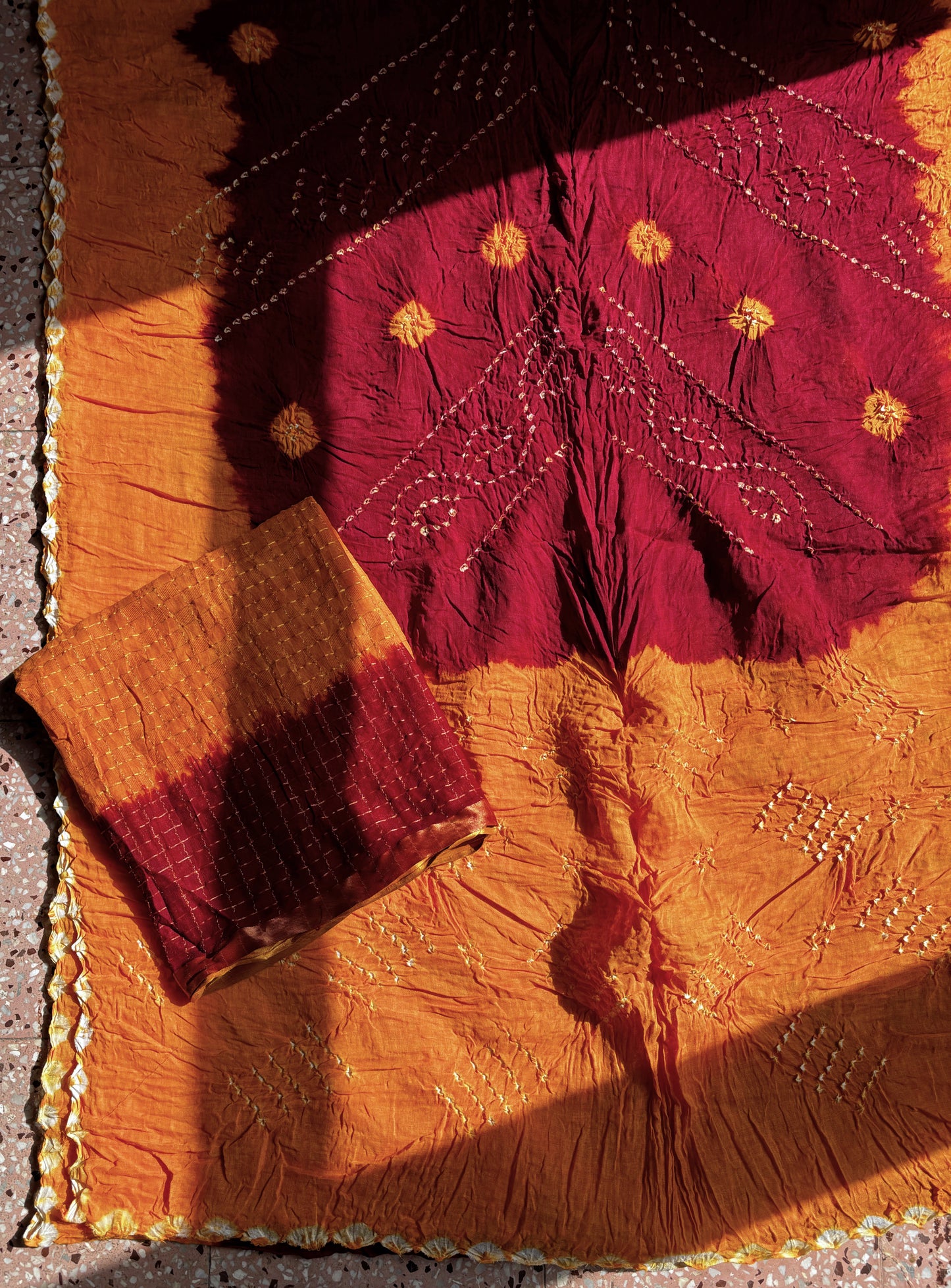 Marigold orange and deep maroon hand tie-dyed Bandhani cotton saree with floral and geometric motifs
