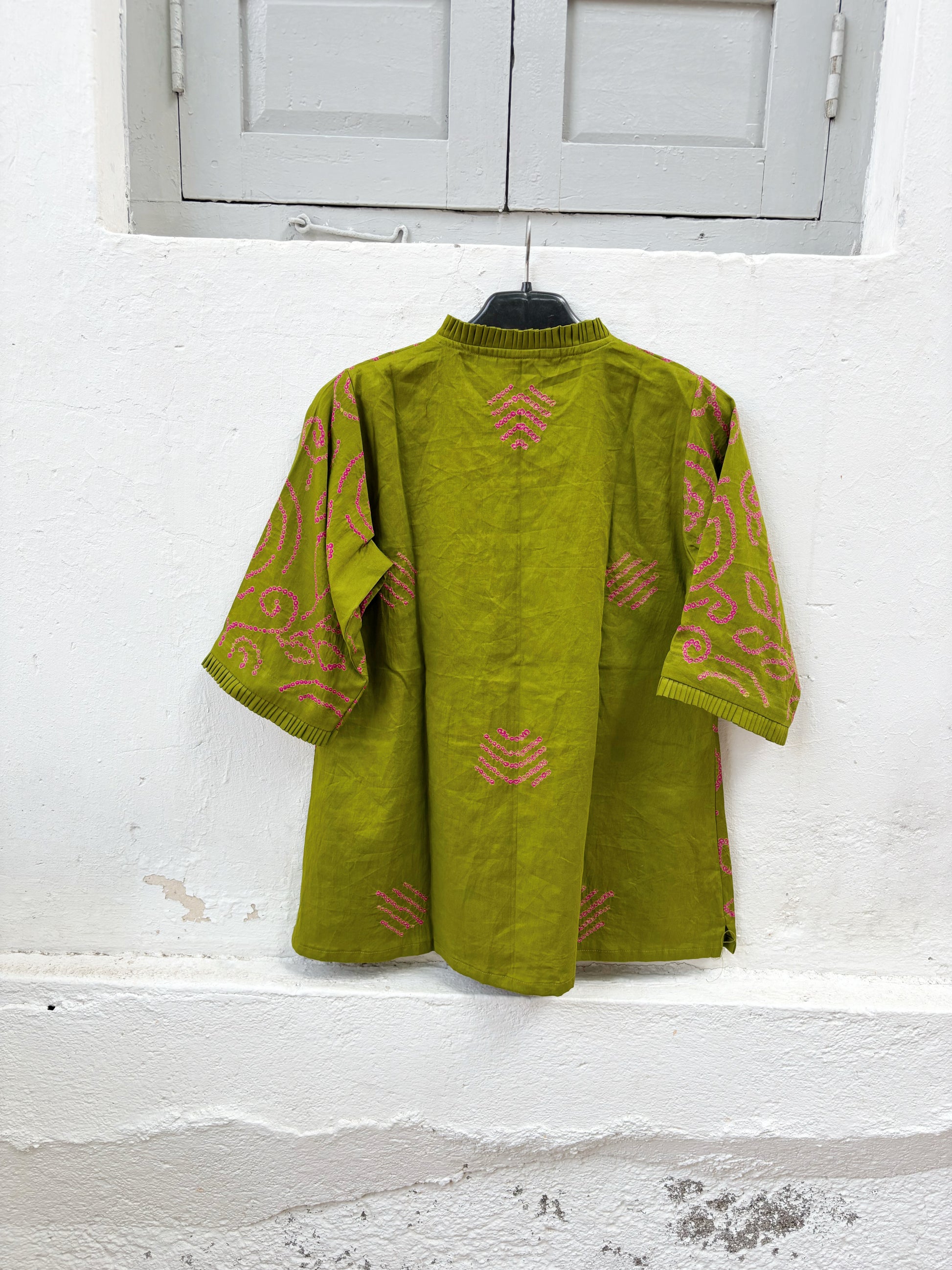 Olive green Jhankar Bandhani cotton shirt with rani pink floral and paisley motifs, pleated neckline, pleated sleeve hems, coconut shell buttons, and relaxed fit.