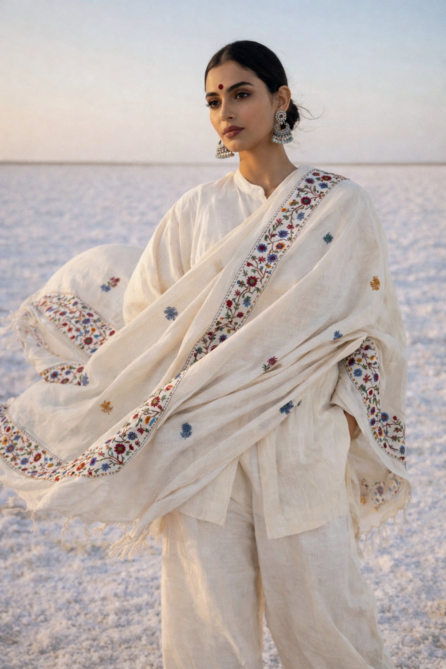 Handspun cotton dupatta in warm ivory shade featuring continuous floral hand embroidery along the borders in red, blue, mustard, and green. Lightweight handcrafted dupatta with tassel edges, named Pallavi.