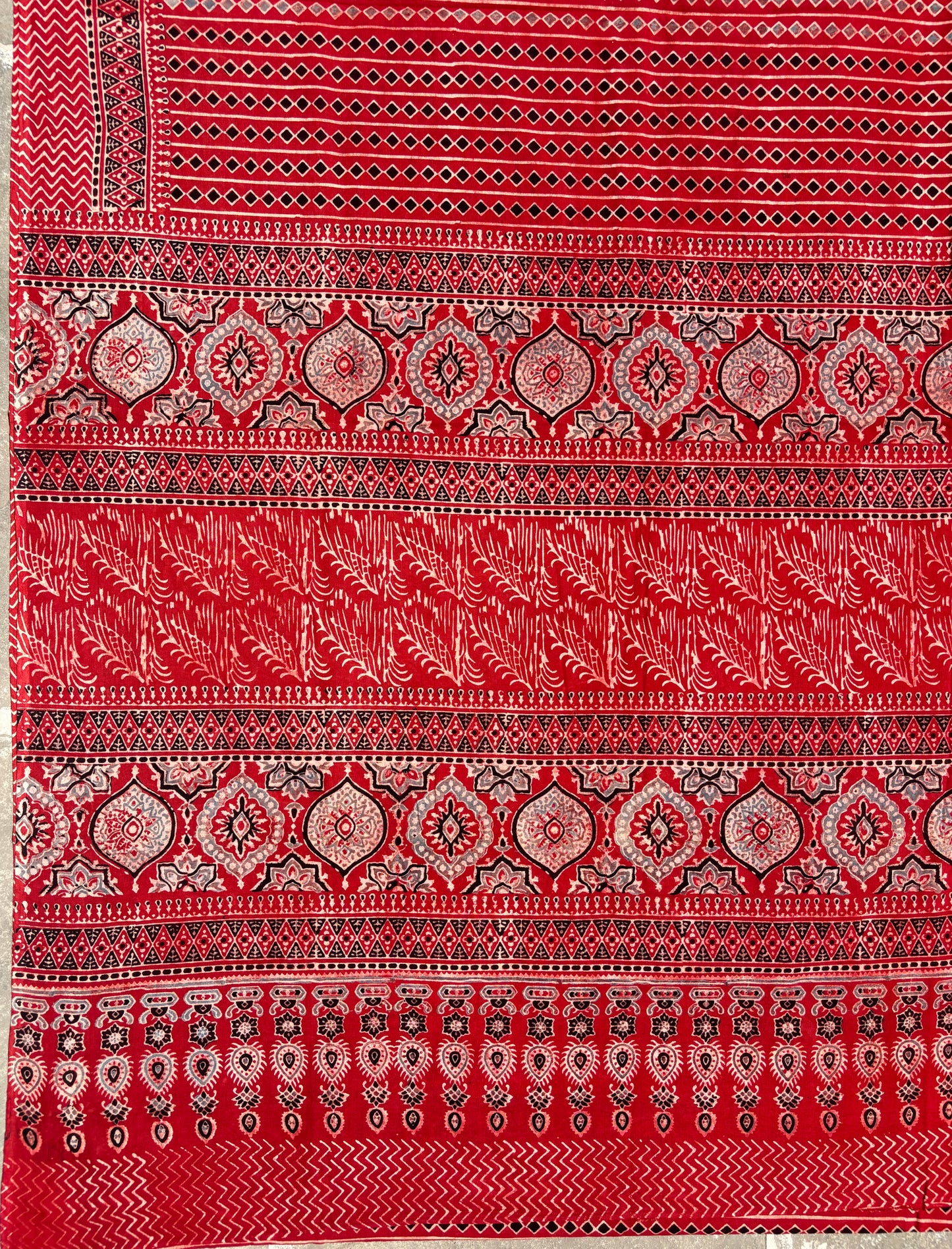 Madder dyed cotton Ajrakh hand block printed saree featuring traditional geometric motifs in red, black, and beige with detailed borders and pallu.