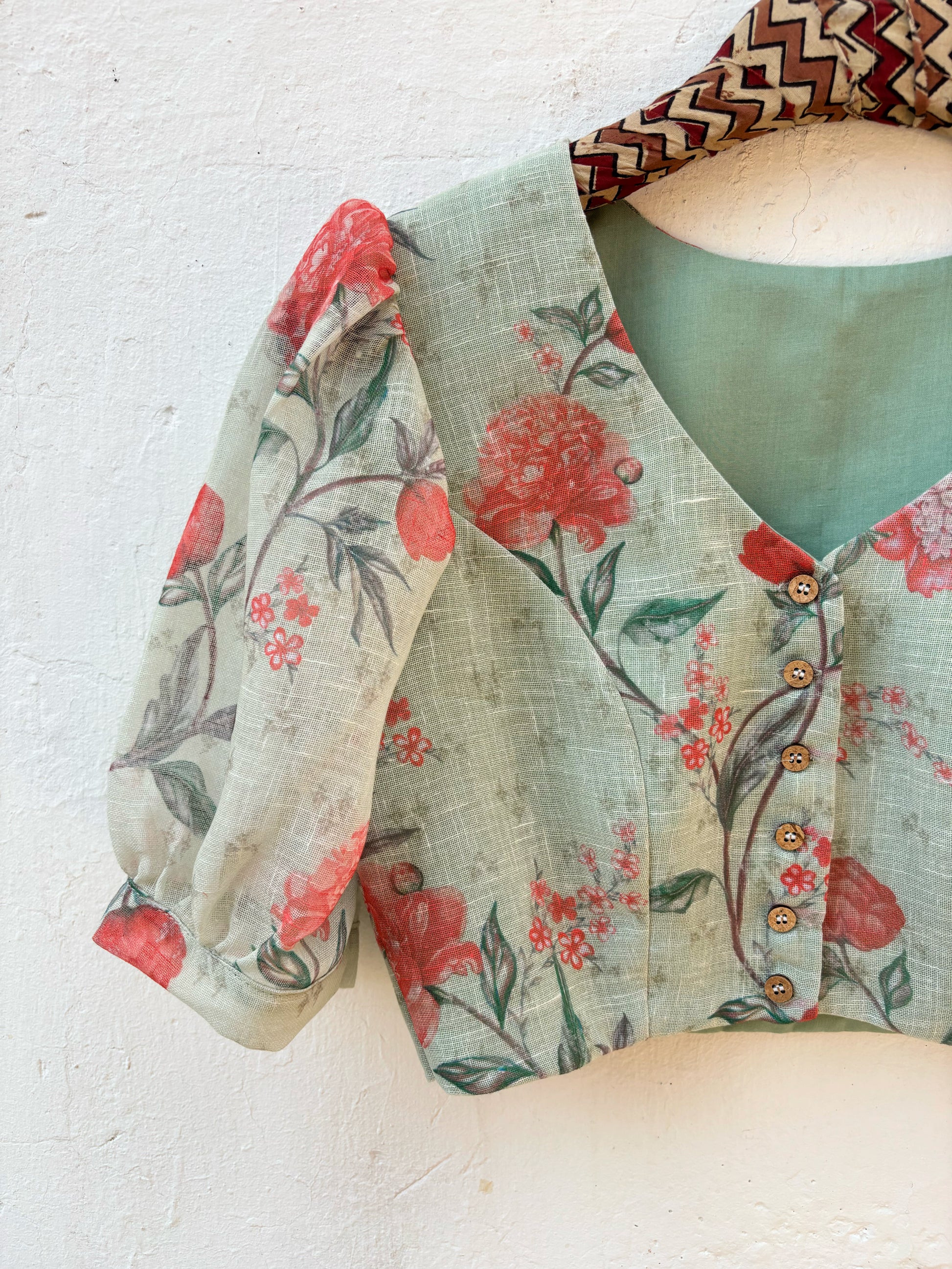 Slow-made sage green floral linen blouse with curved V-neck, front wooden buttons and subtle puff sleeves, fully lined and consciously crafted in India.
