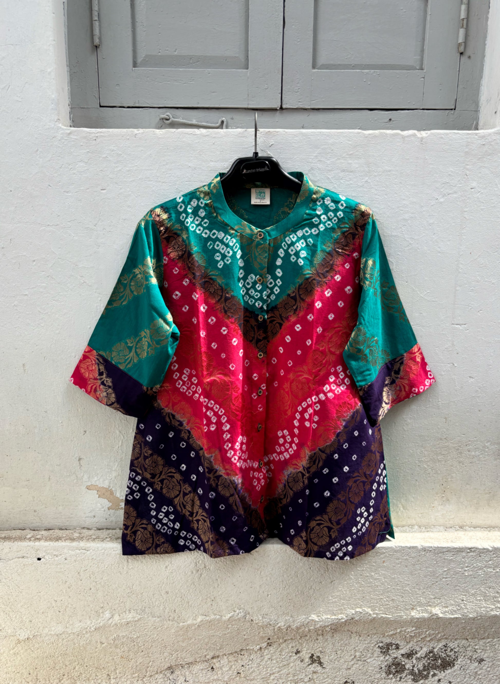 Handcrafted Bandhani festive cotton shirt in Peacock Blue, Fuchsia Pink and Royal Purple with antique gold woven floral motifs, round band neckline, short button placket, relaxed fit and three-quarter sleeves.
