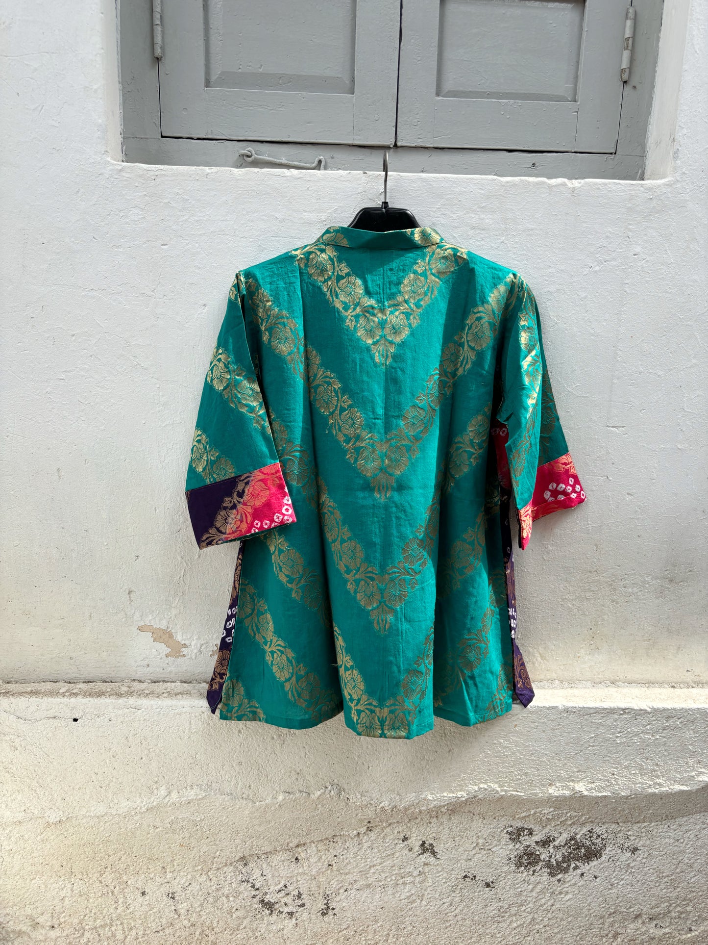 Handcrafted Bandhani festive cotton shirt in Peacock Blue, Fuchsia Pink and Royal Purple with antique gold woven floral motifs, round band neckline, short button placket, relaxed fit and three-quarter sleeves.
