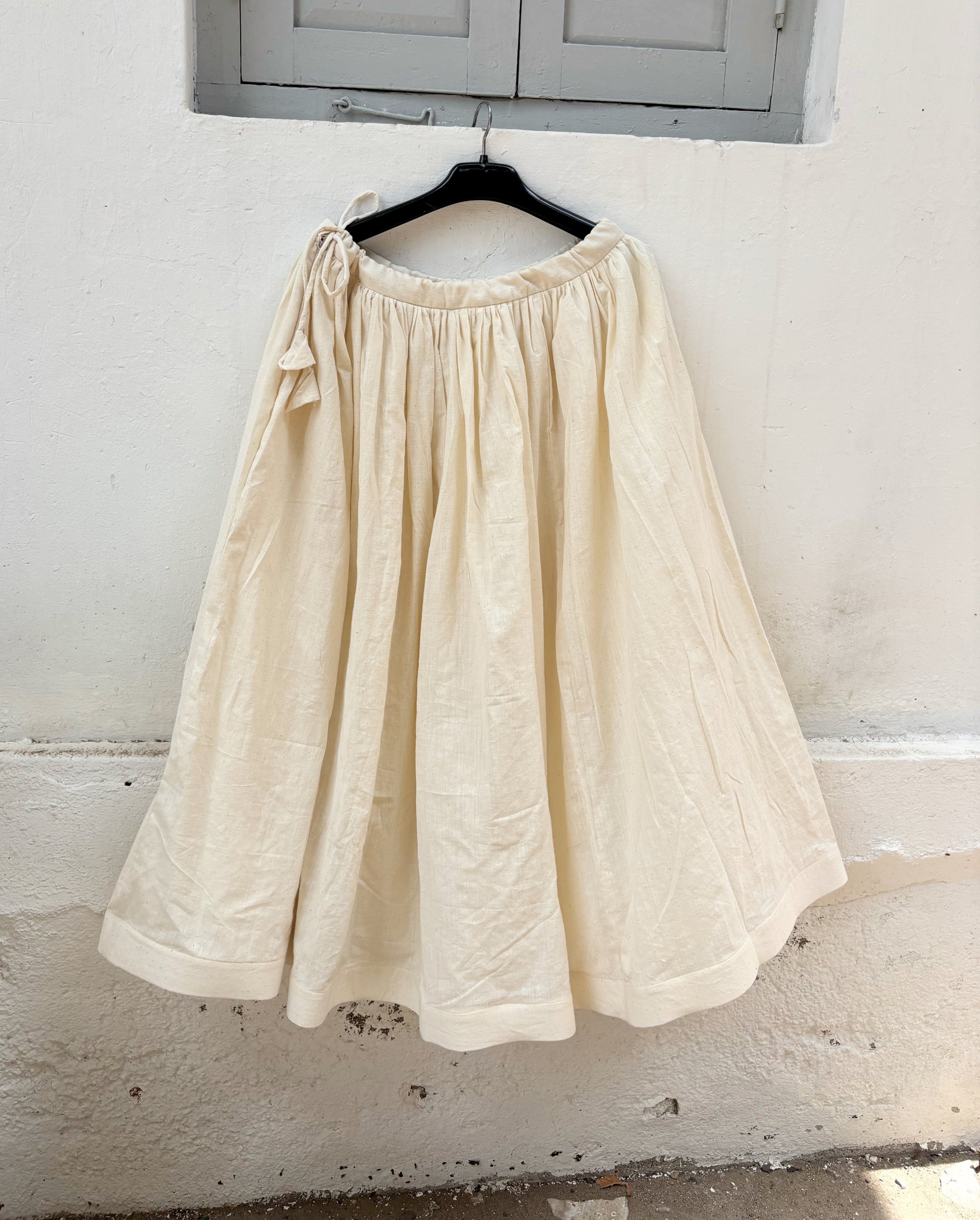 Undyed raw hand-spun and handwoven cotton gathered skirt in natural off-white with adjustable tie strings, side zipper and flowing silhouette.